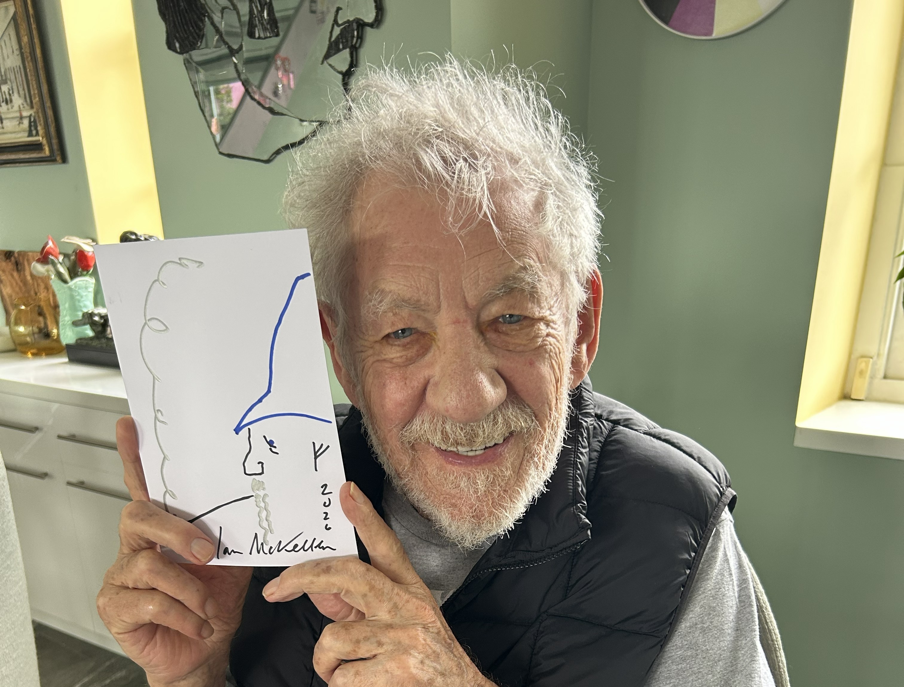 Smiling elderly man holding a hand-drawn card with a wizard illustration