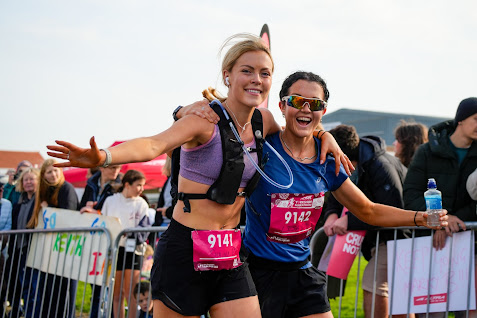 Two women runners smiling and celebrating at finish line