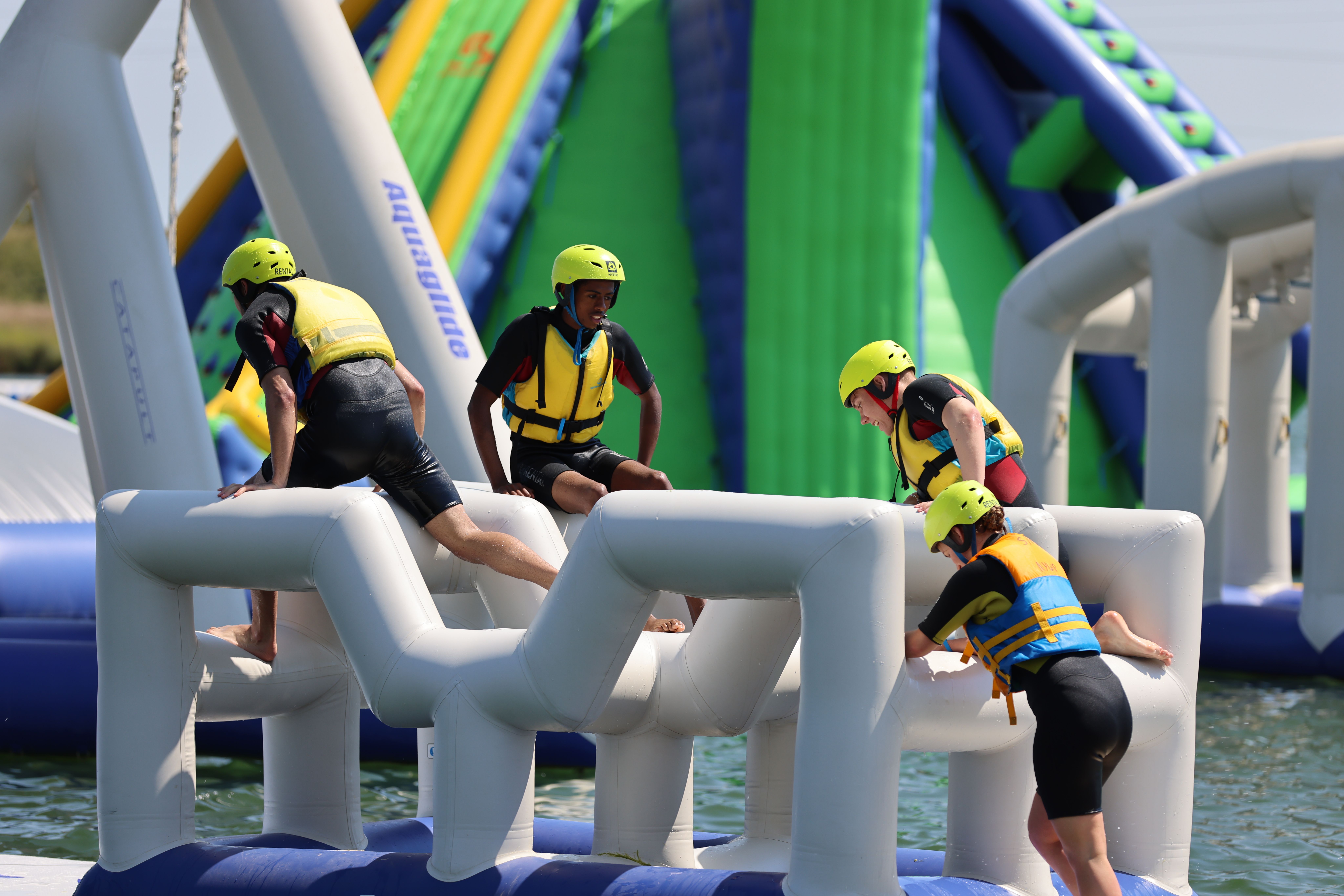 People in helmets navigating inflatable water obstacle course