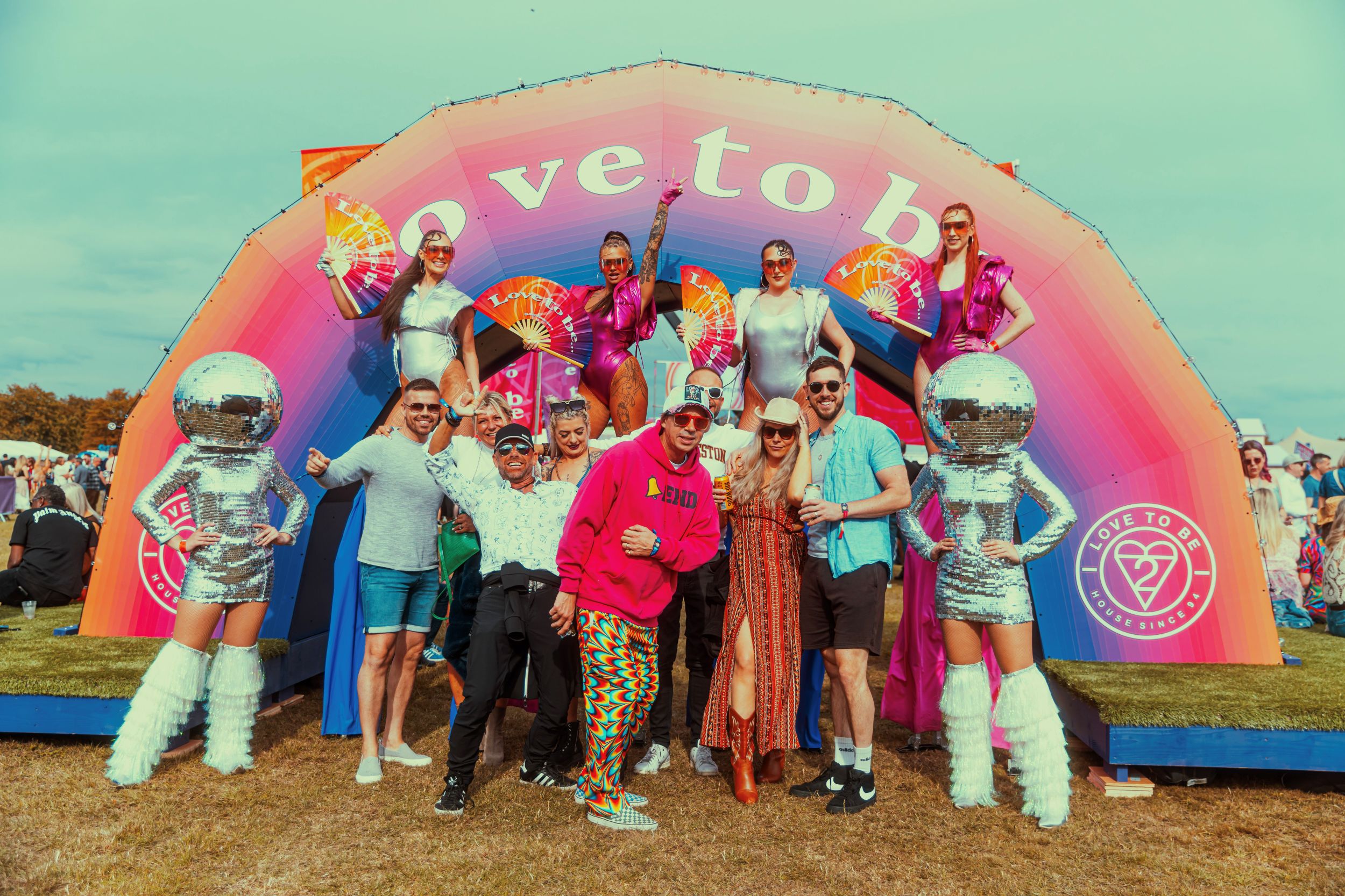 Festival goers in colorful outfits under vibrant rainbow arch