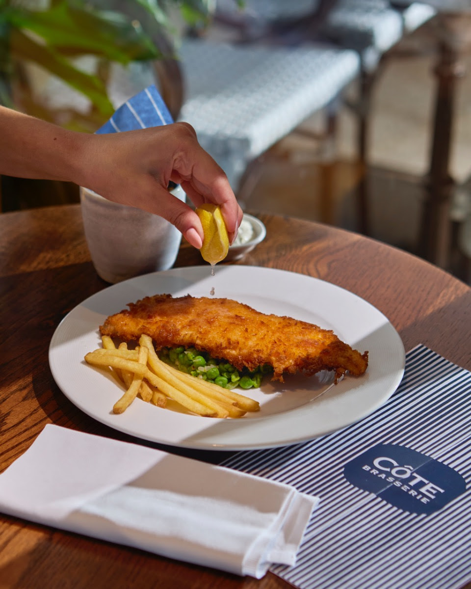 Hand squeezing lemon over fish and chips at restaurant table