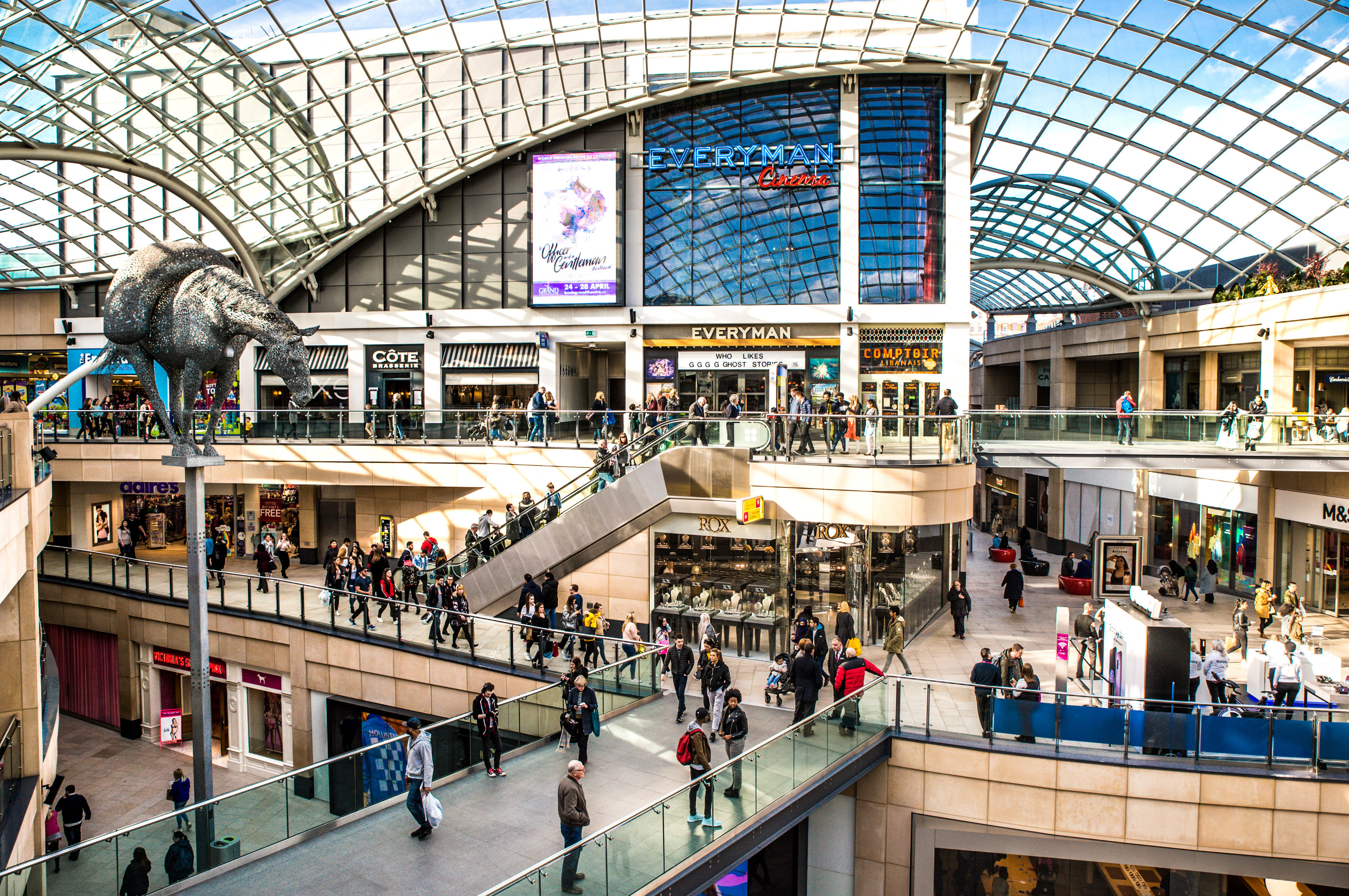 Modern shopping centre with glass roof and large crowd