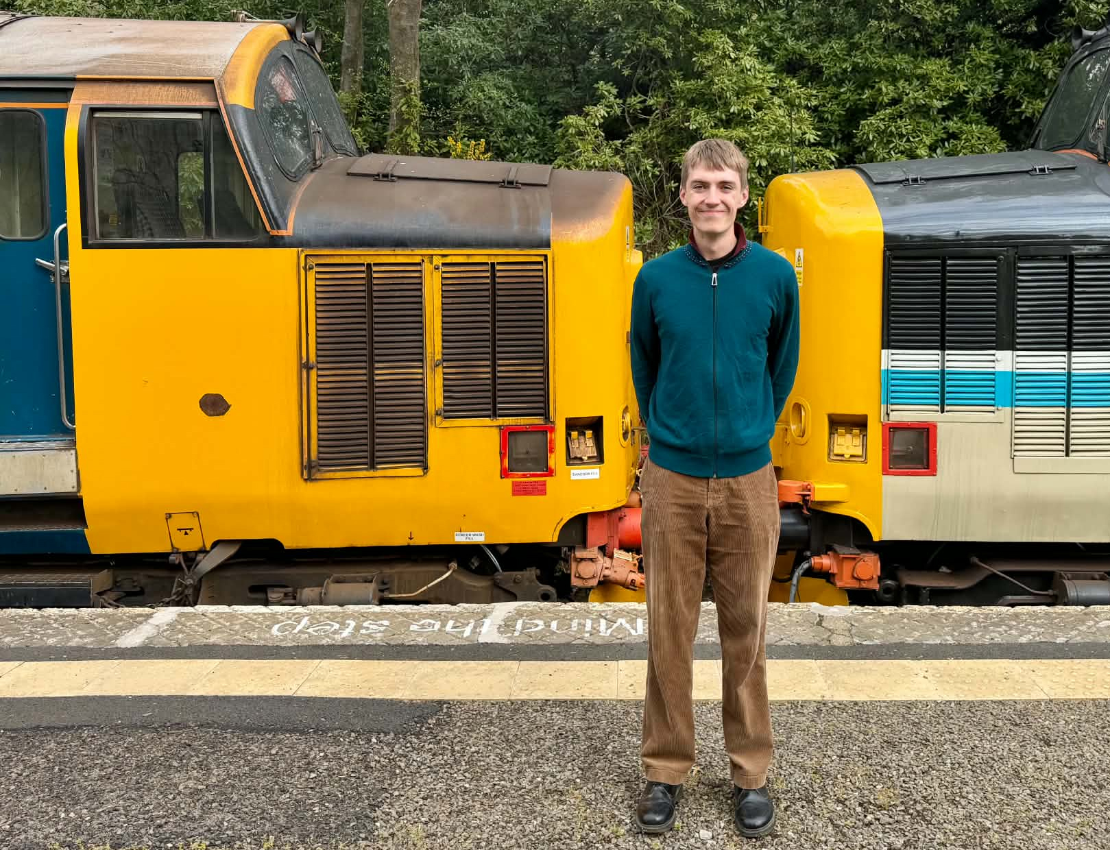 Man in green jacket standing by vintage yellow trains at station