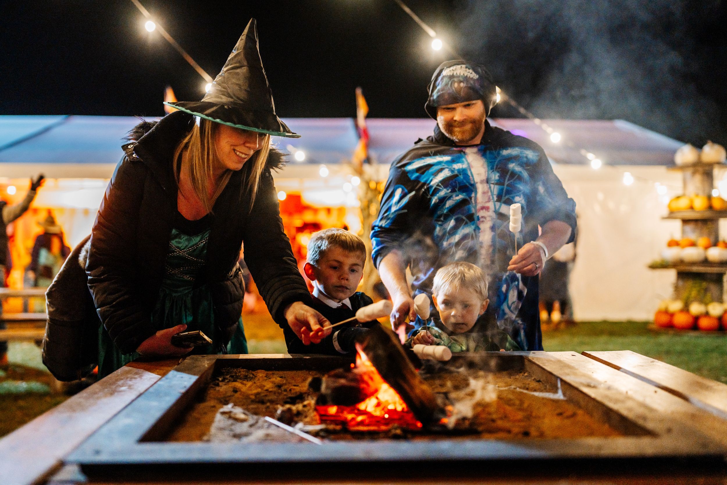 Family in Halloween costumes roasting marshmallows at night festival