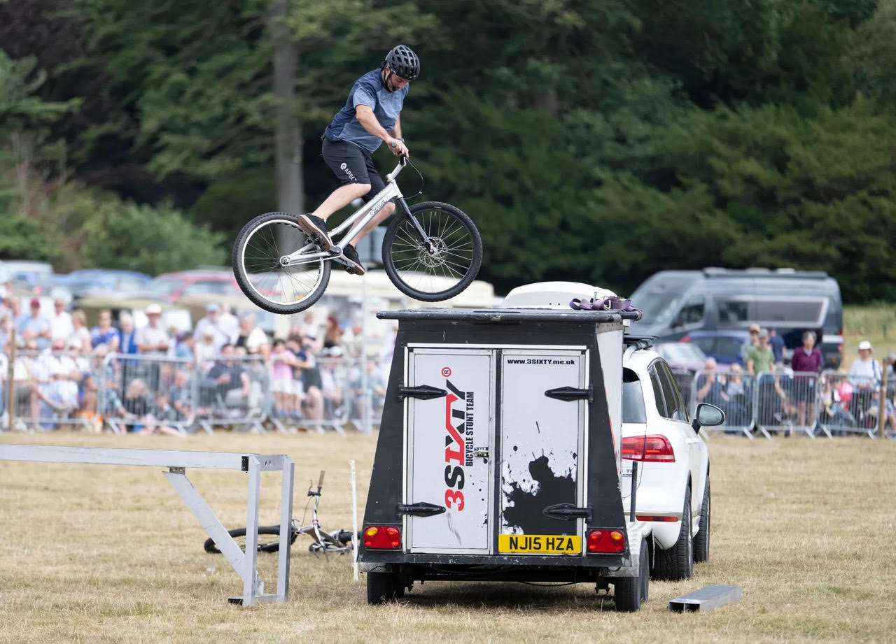 Cyclist performing a stunt on a bike over a van at an outdoor event