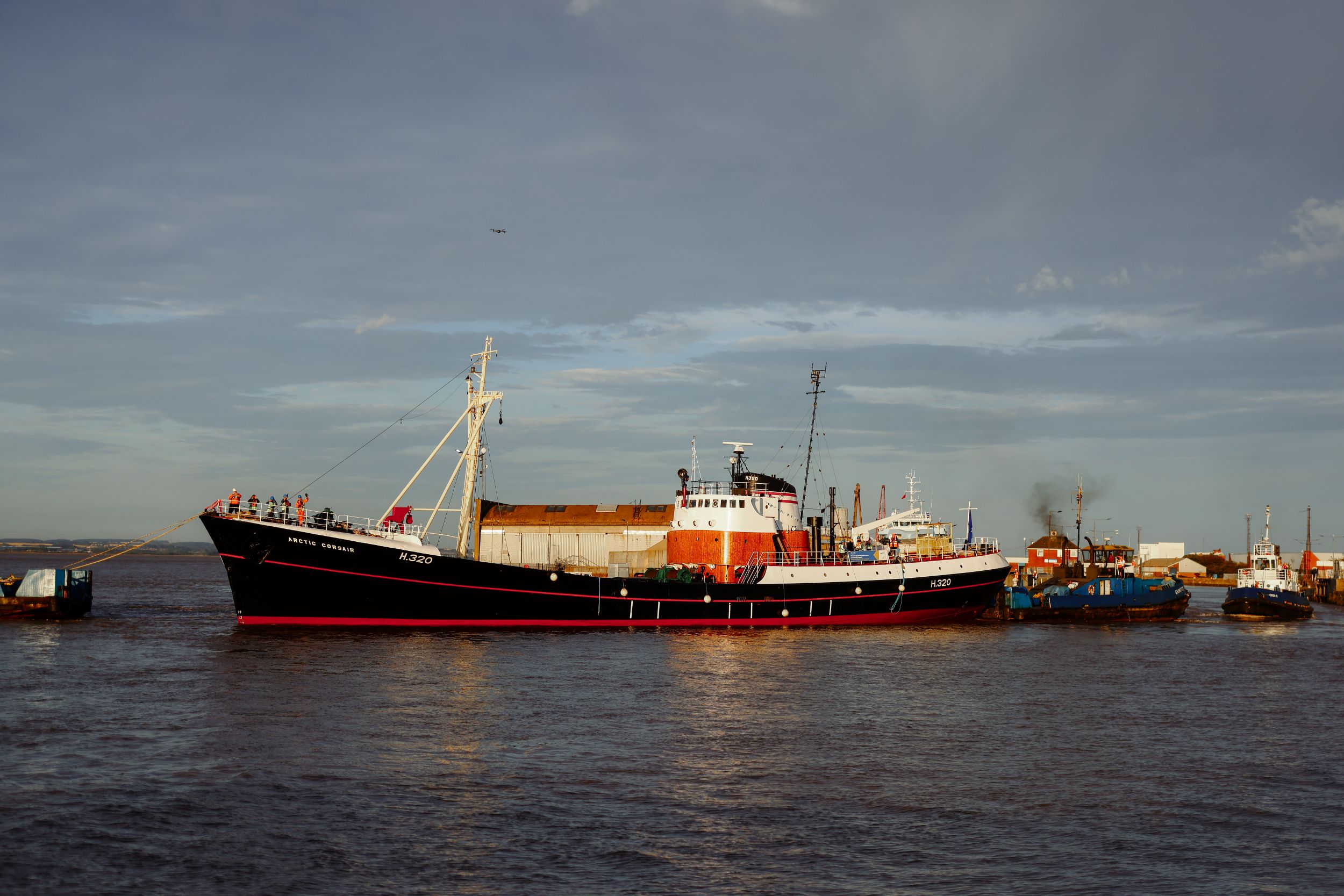 Historic red and black trawler docked with industrial background