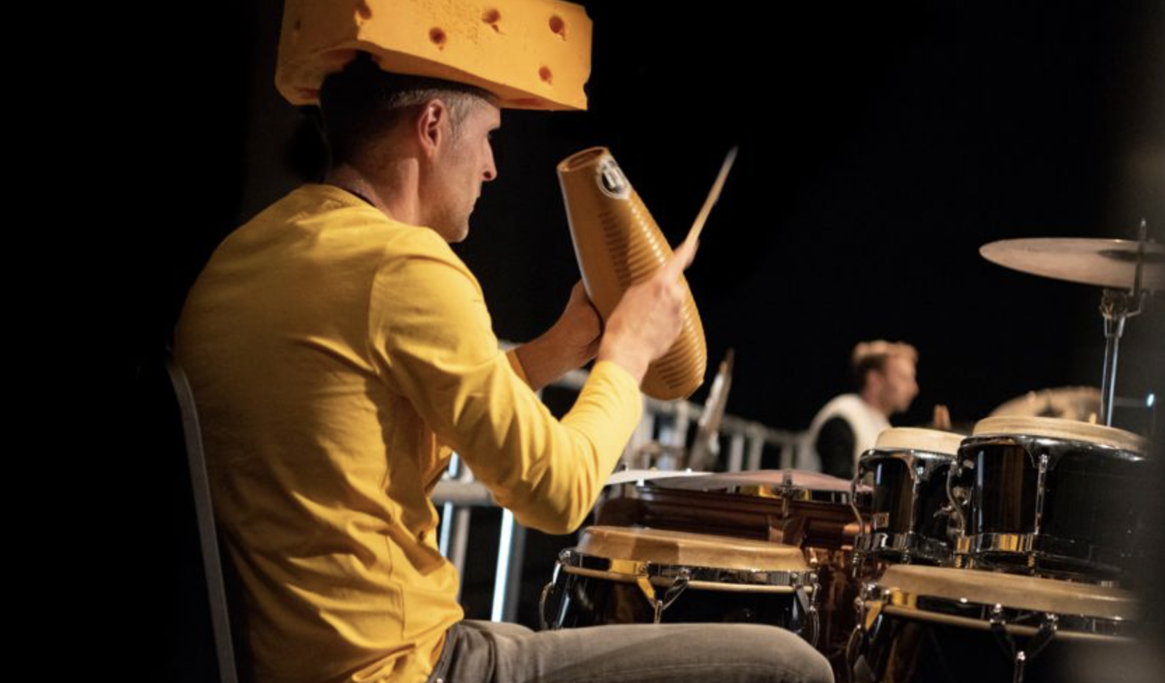 Musician in yellow shirt playing percussion with cheese hat