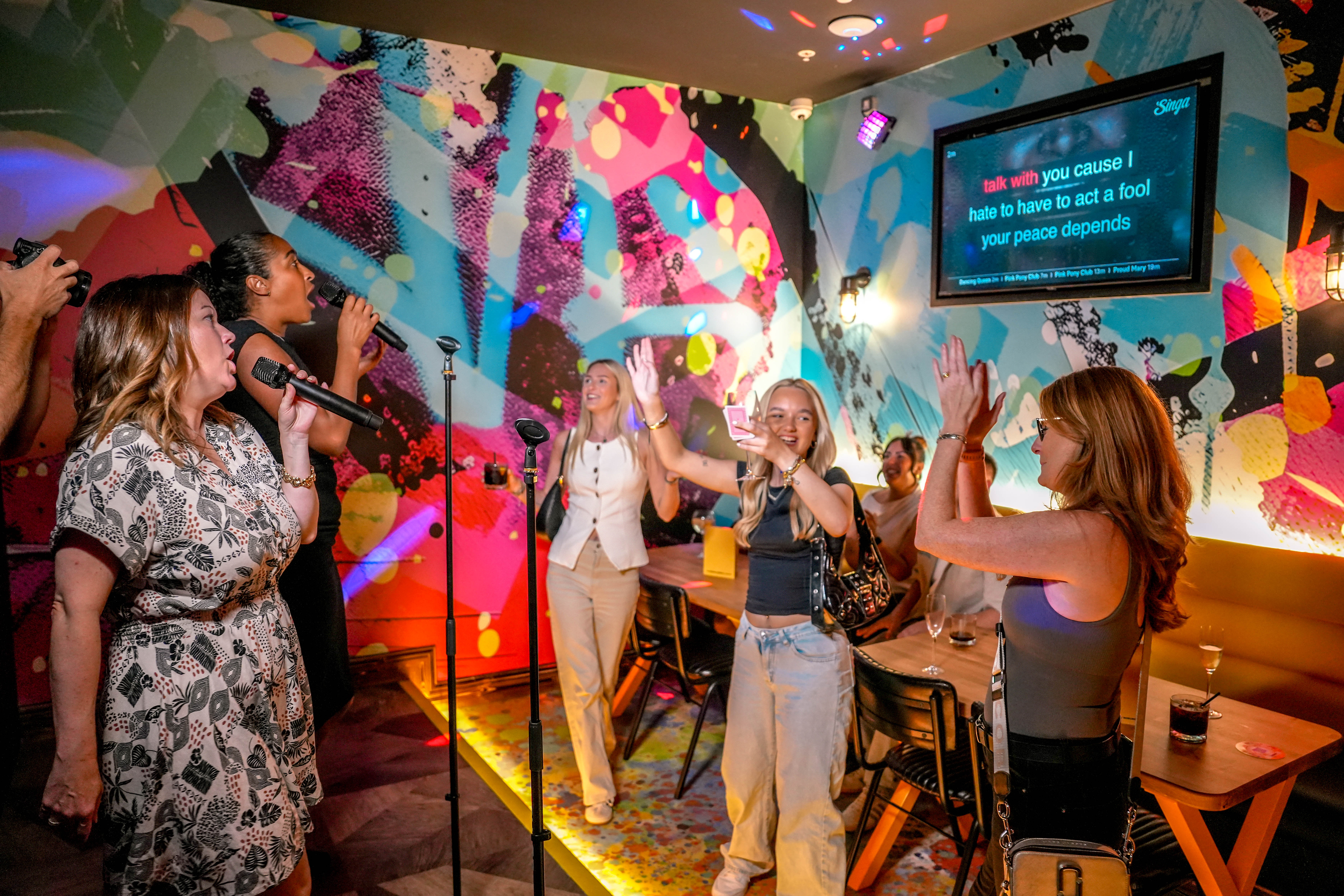 Group of friends singing karaoke in colourful room with mural walls