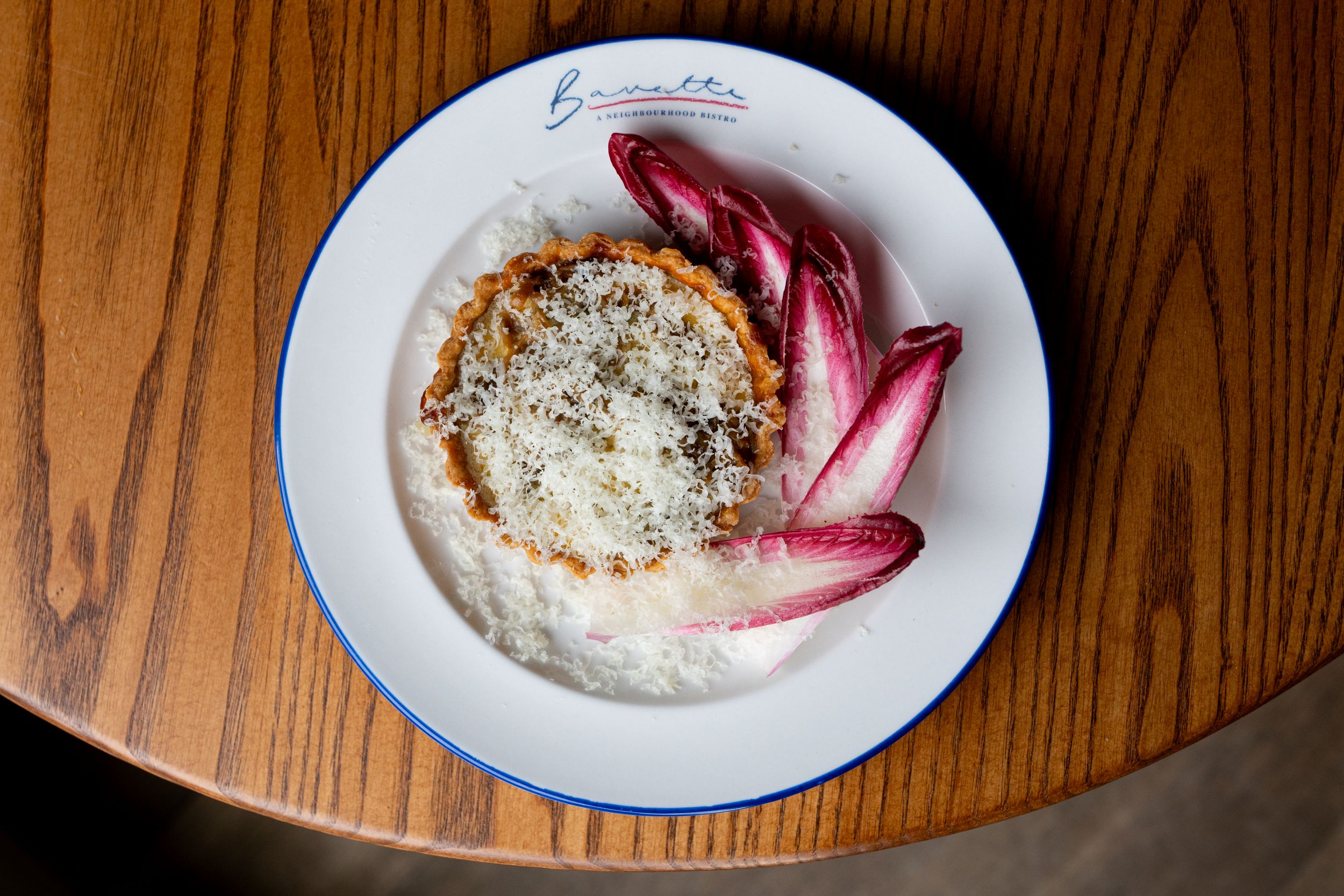Cheese tart with grated cheese and red chicory on a wooden table