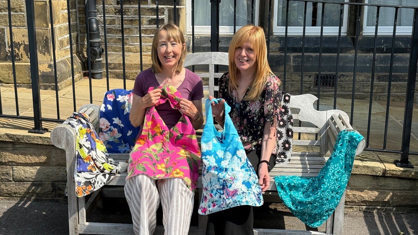 Two women seated on a bench displaying colourful handmade bags