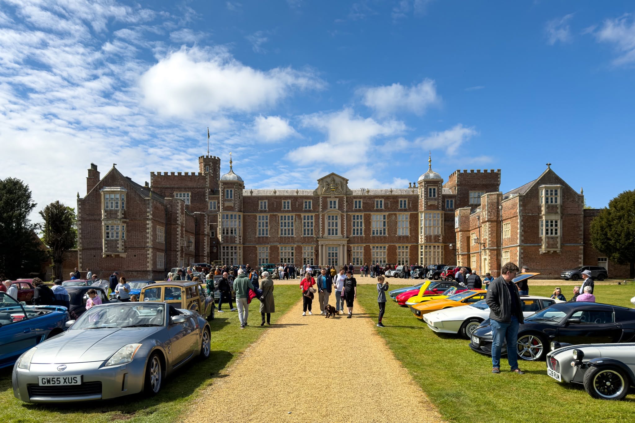Historic brick mansion with visitors and classic cars on lawn