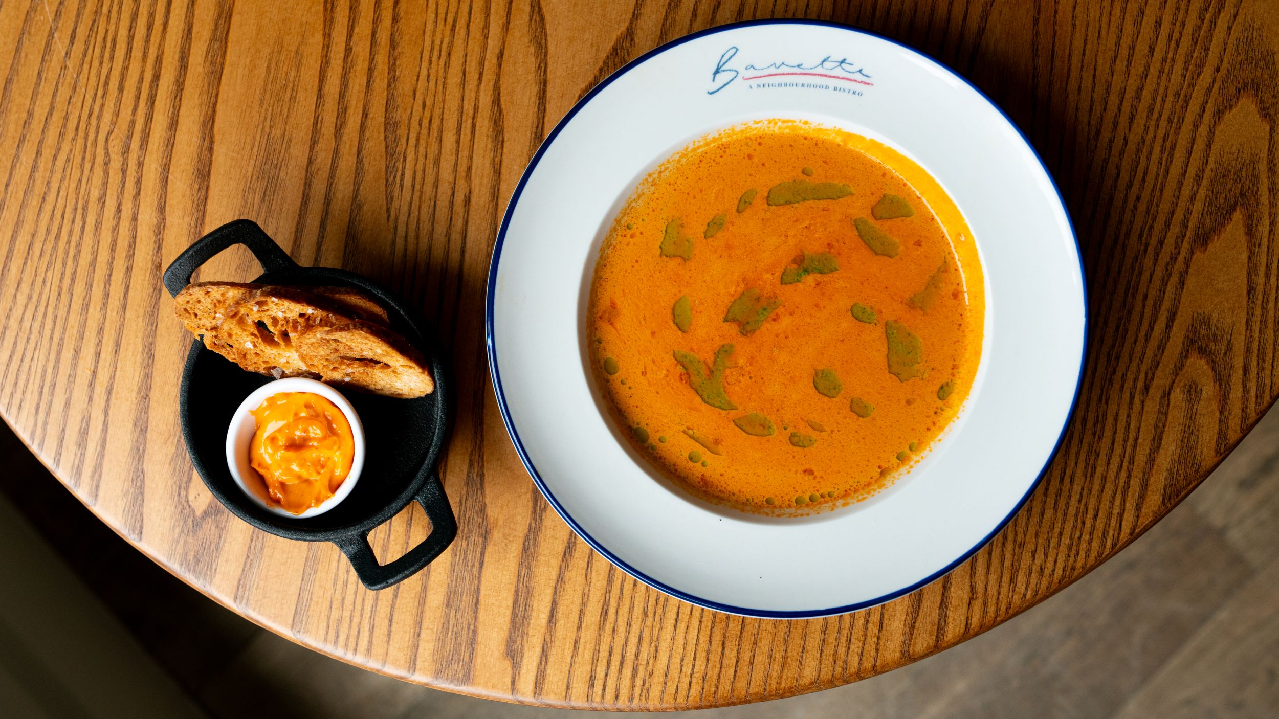 Tomato soup with herb oil swirl and bread on wooden table
