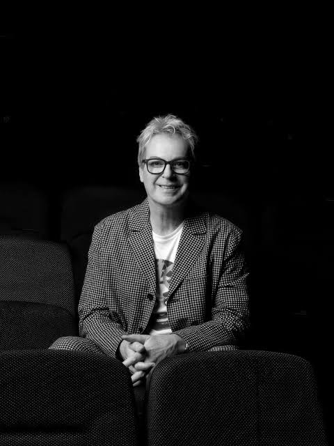 Person seated in a theatre wearing a patterned suit and glasses