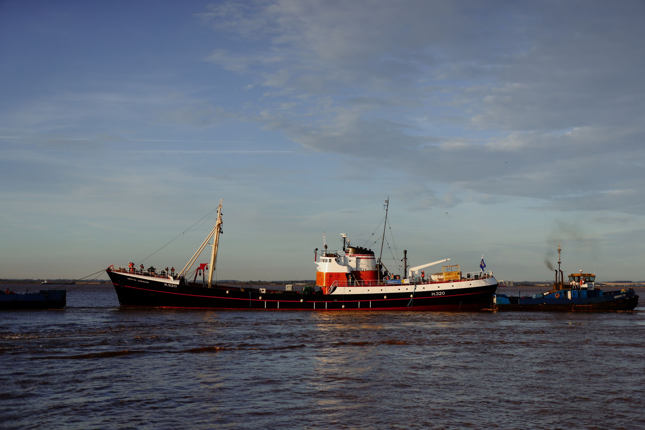 Red and white vintage fishing boat on calm river under blue sky