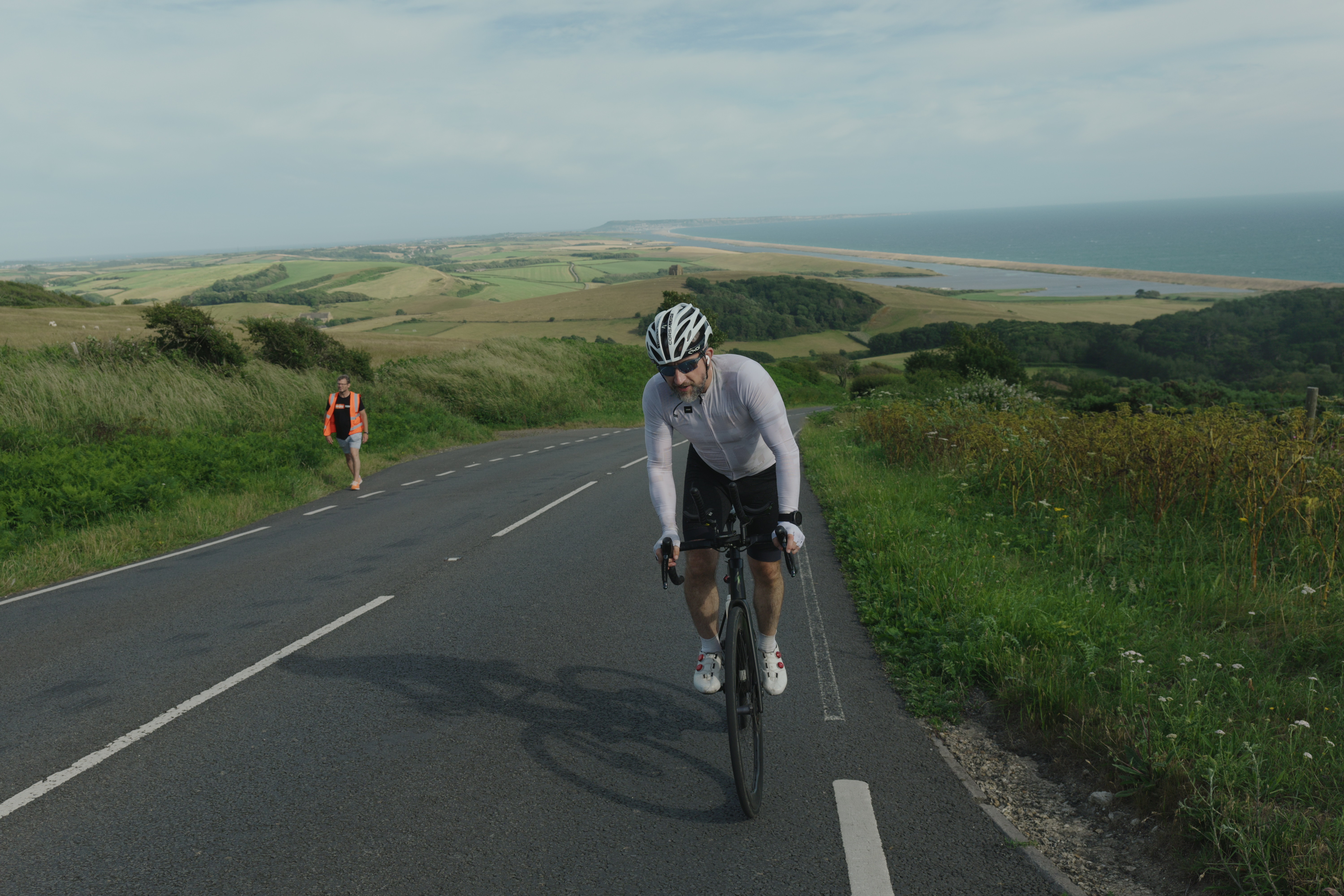 Cyclist on coastal road with rolling green hills and sea