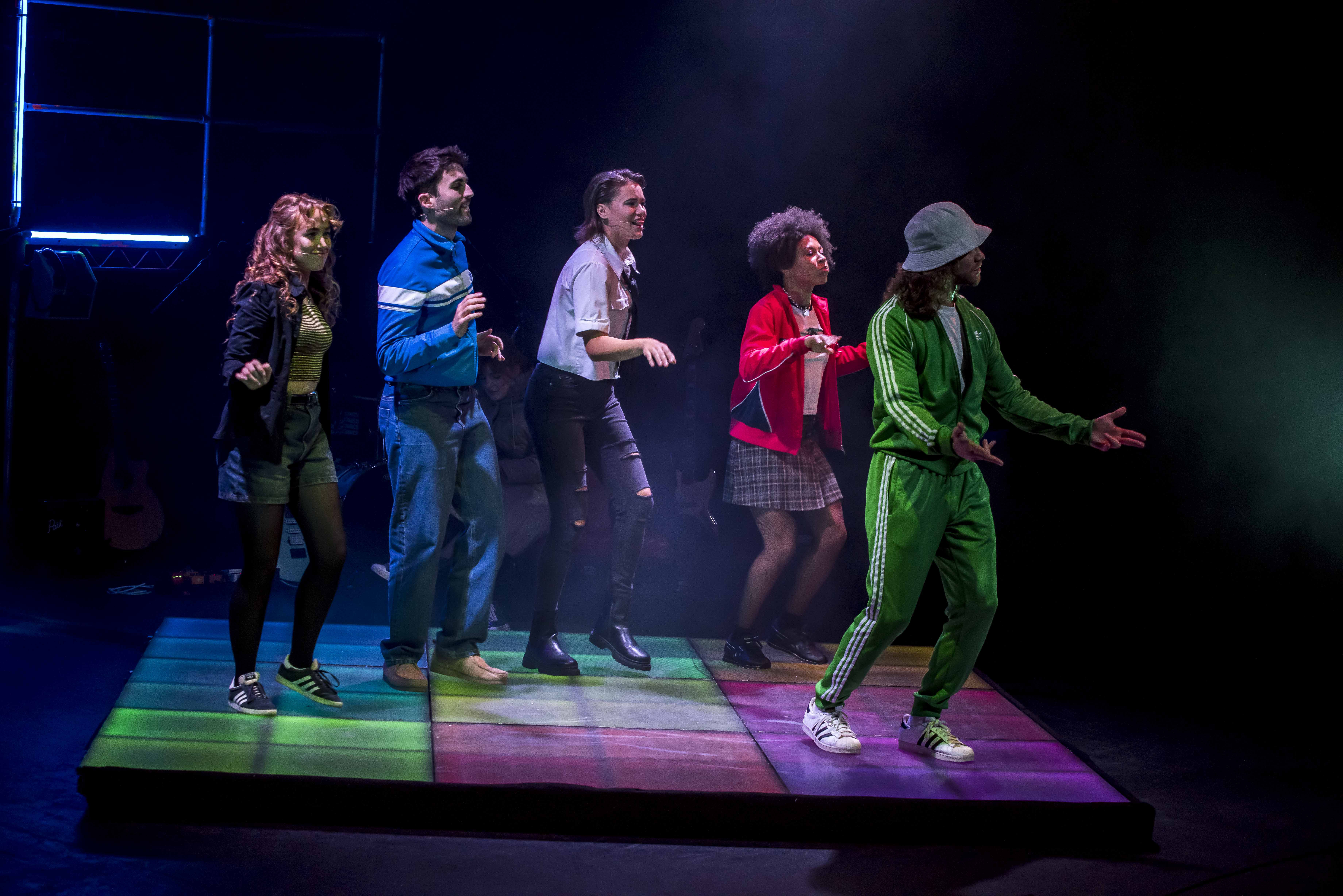 Five performers on a colourful stage in vibrant costumes