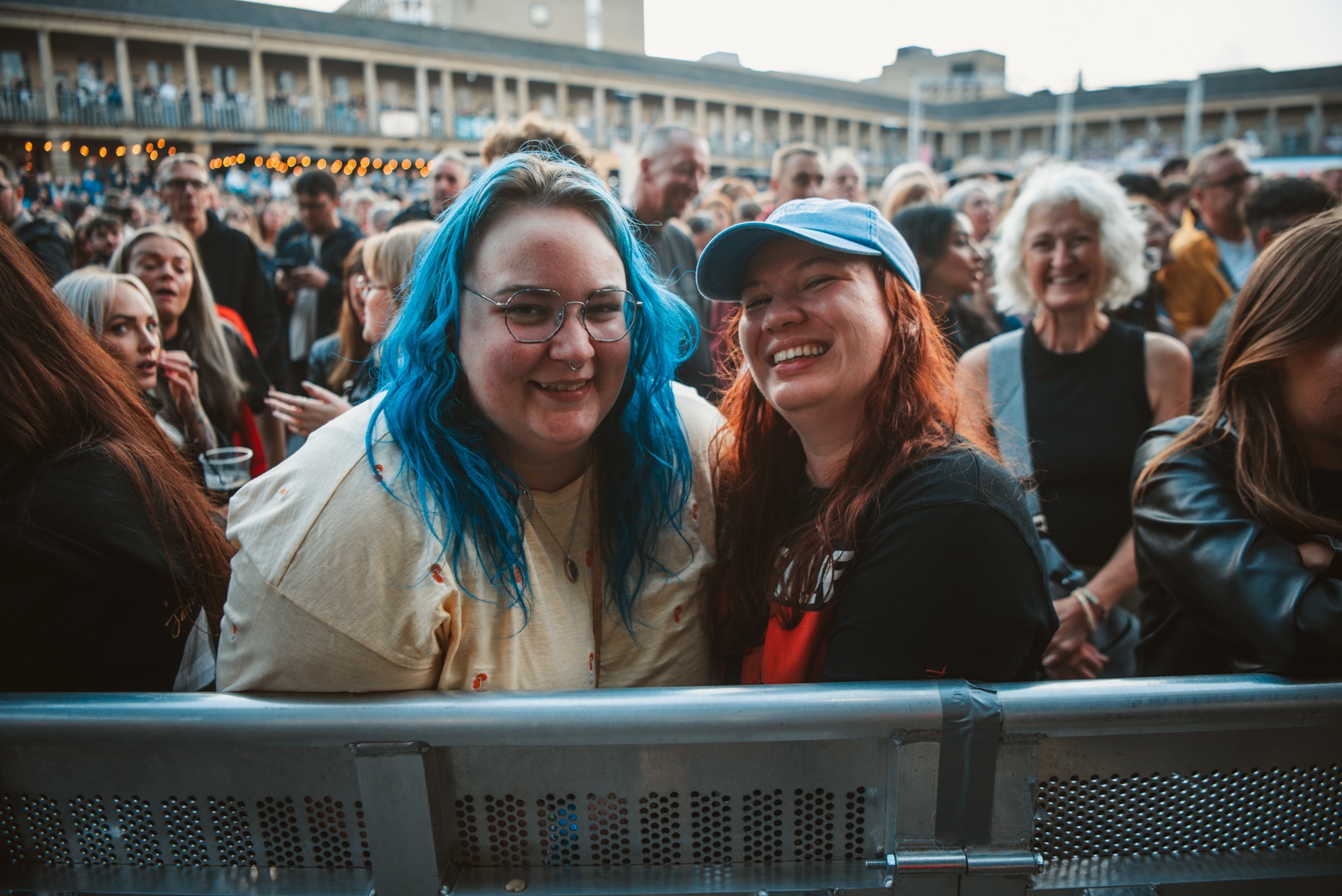 Two smiling women at an outdoor event surrounded by a crowd