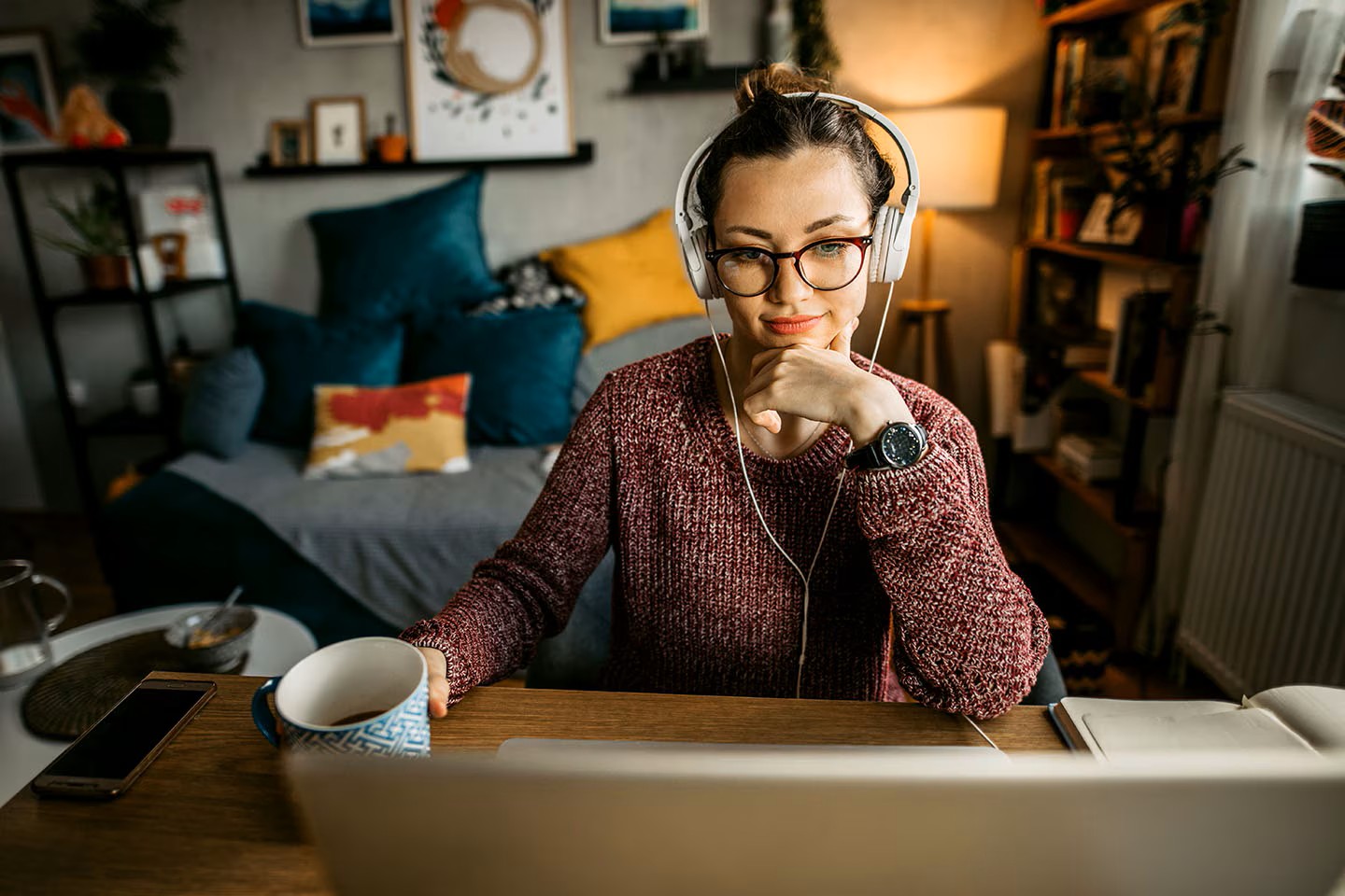 Person in cozy room with headphones and laptop, sipping coffee