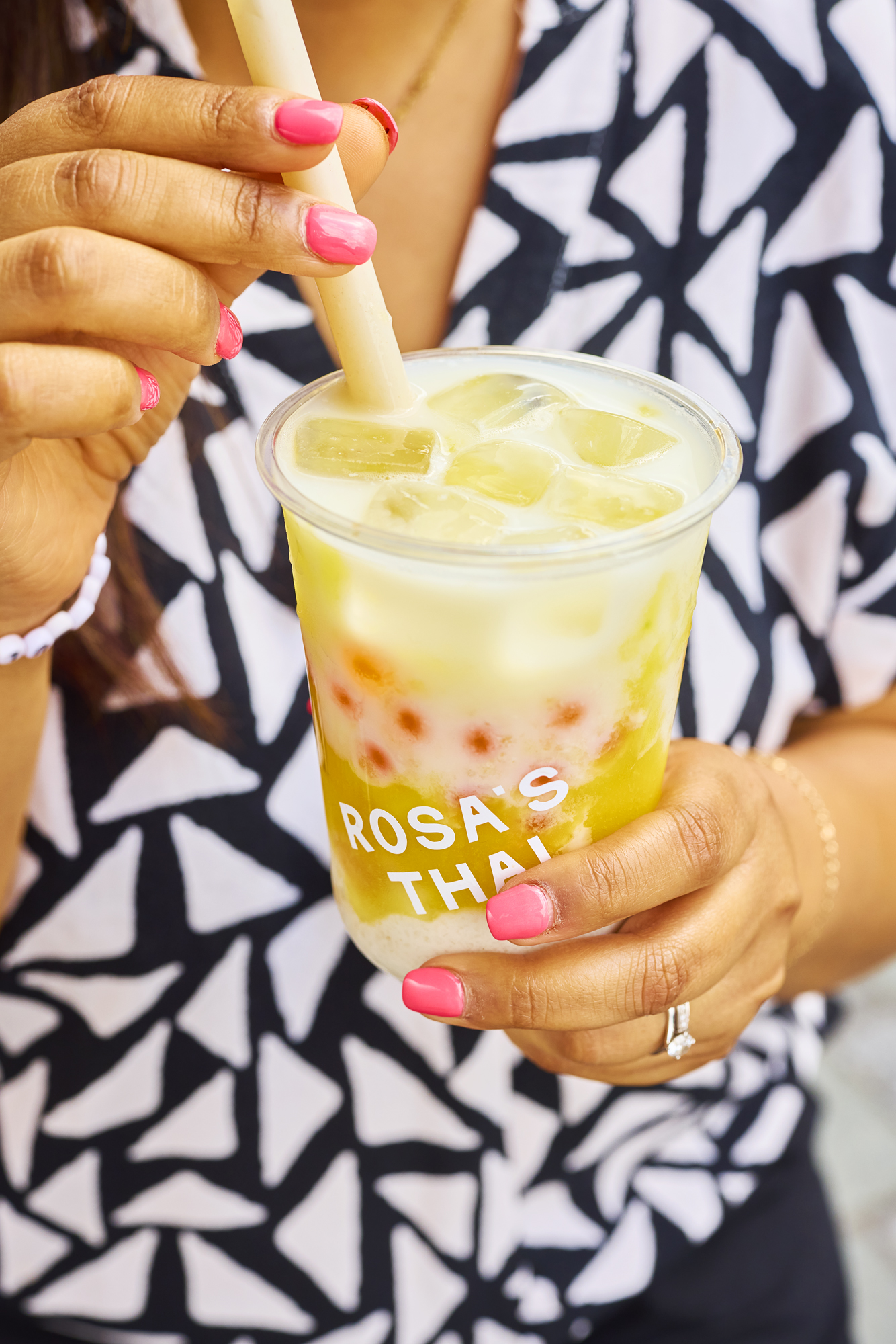 Person holding a cold drink with ice in a clear cup, wearing patterned shirt