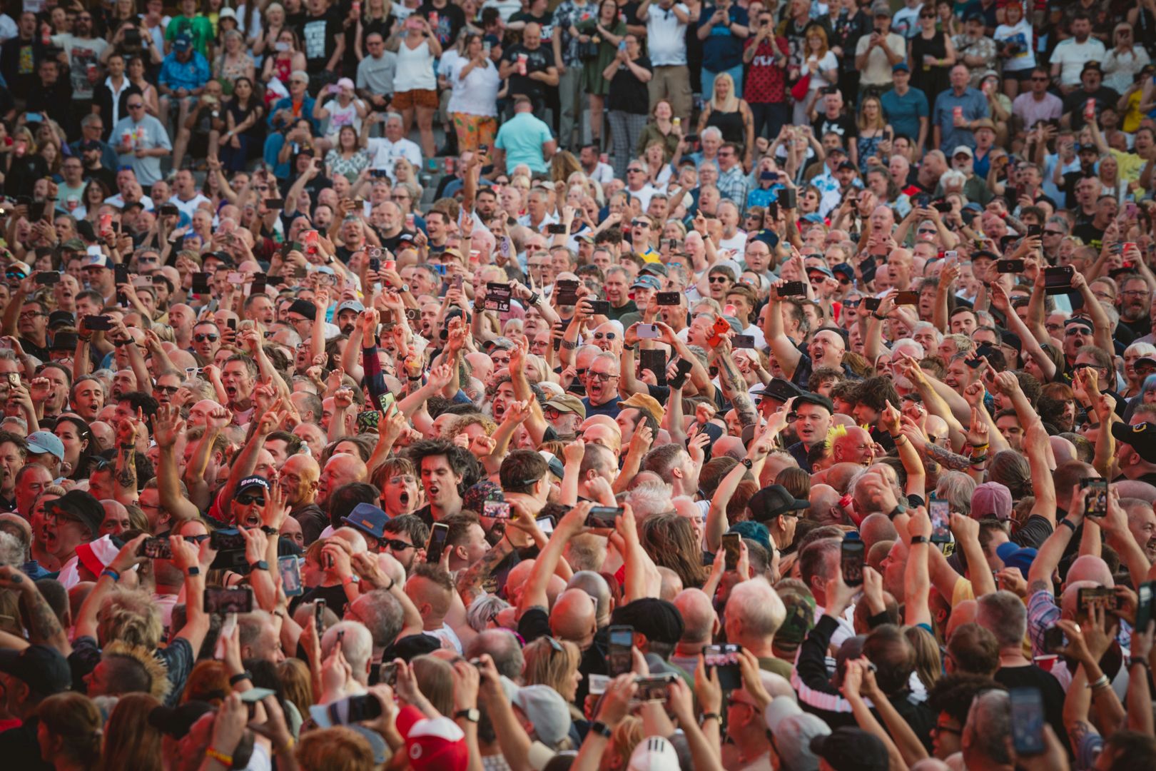 Large crowd of people at an outdoor concert, many holding phones