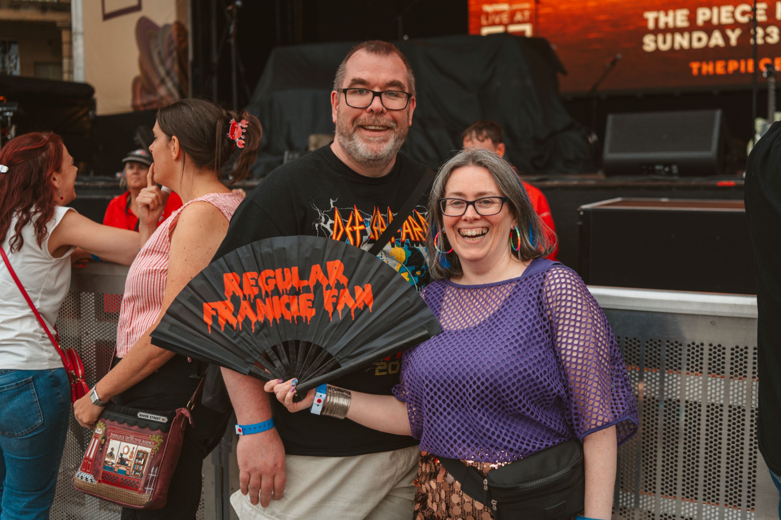 Smiling couple at outdoor music festival holding black fan