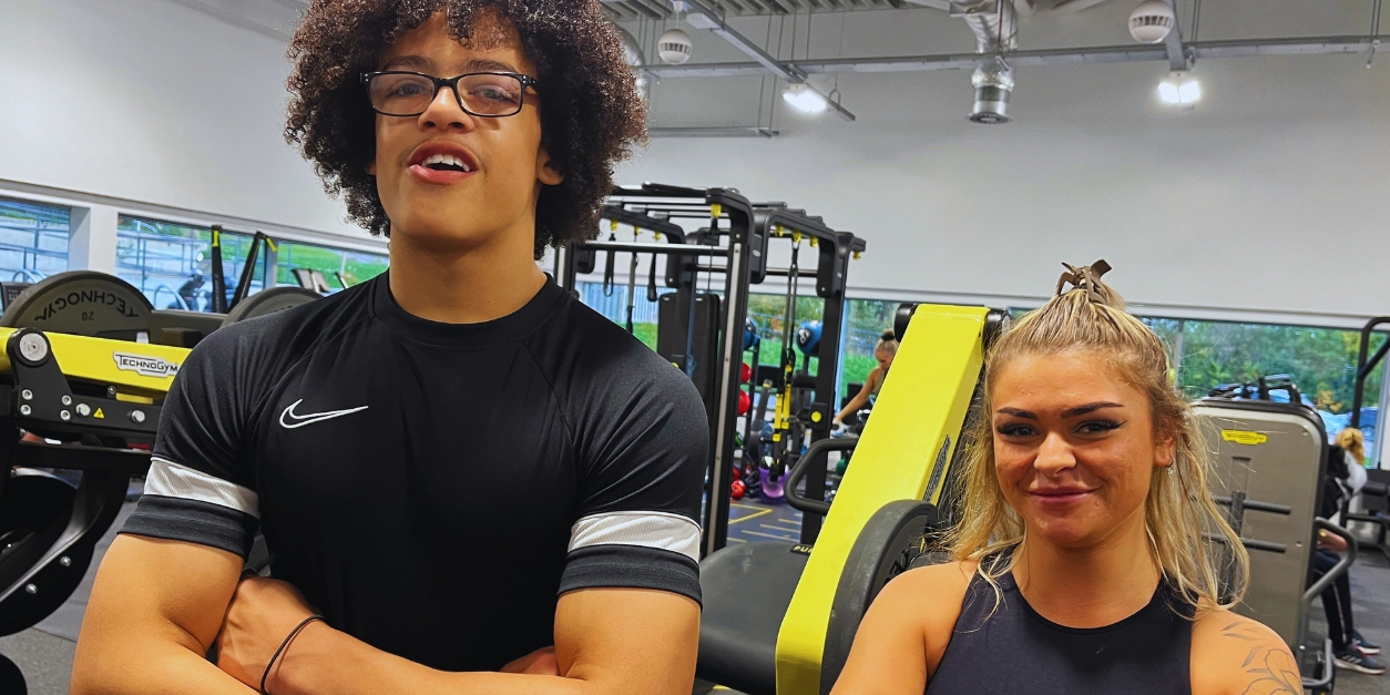 Two people smiling in a modern gym with fitness equipment
