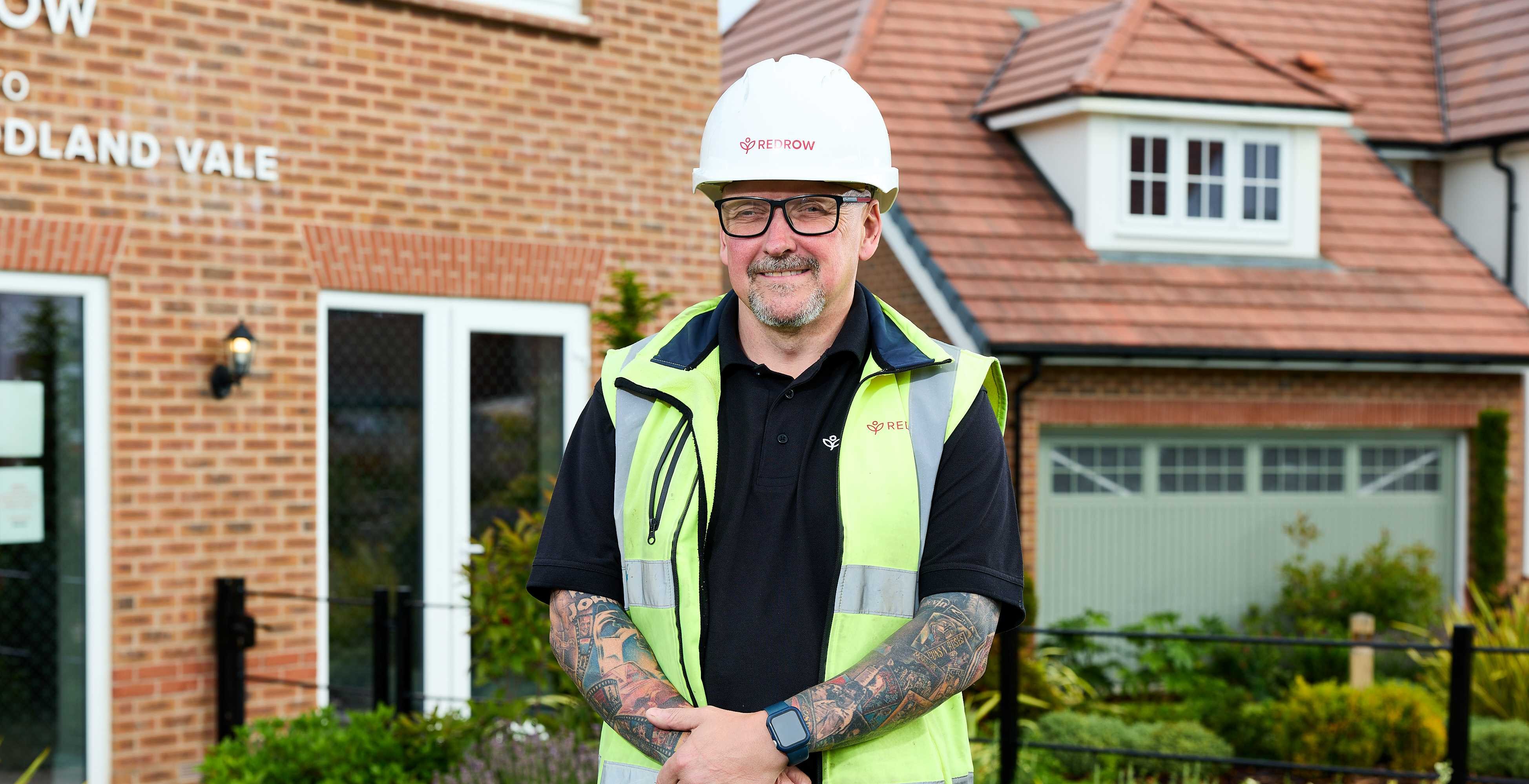 Smiling construction worker in high-vis vest in front of brick houses