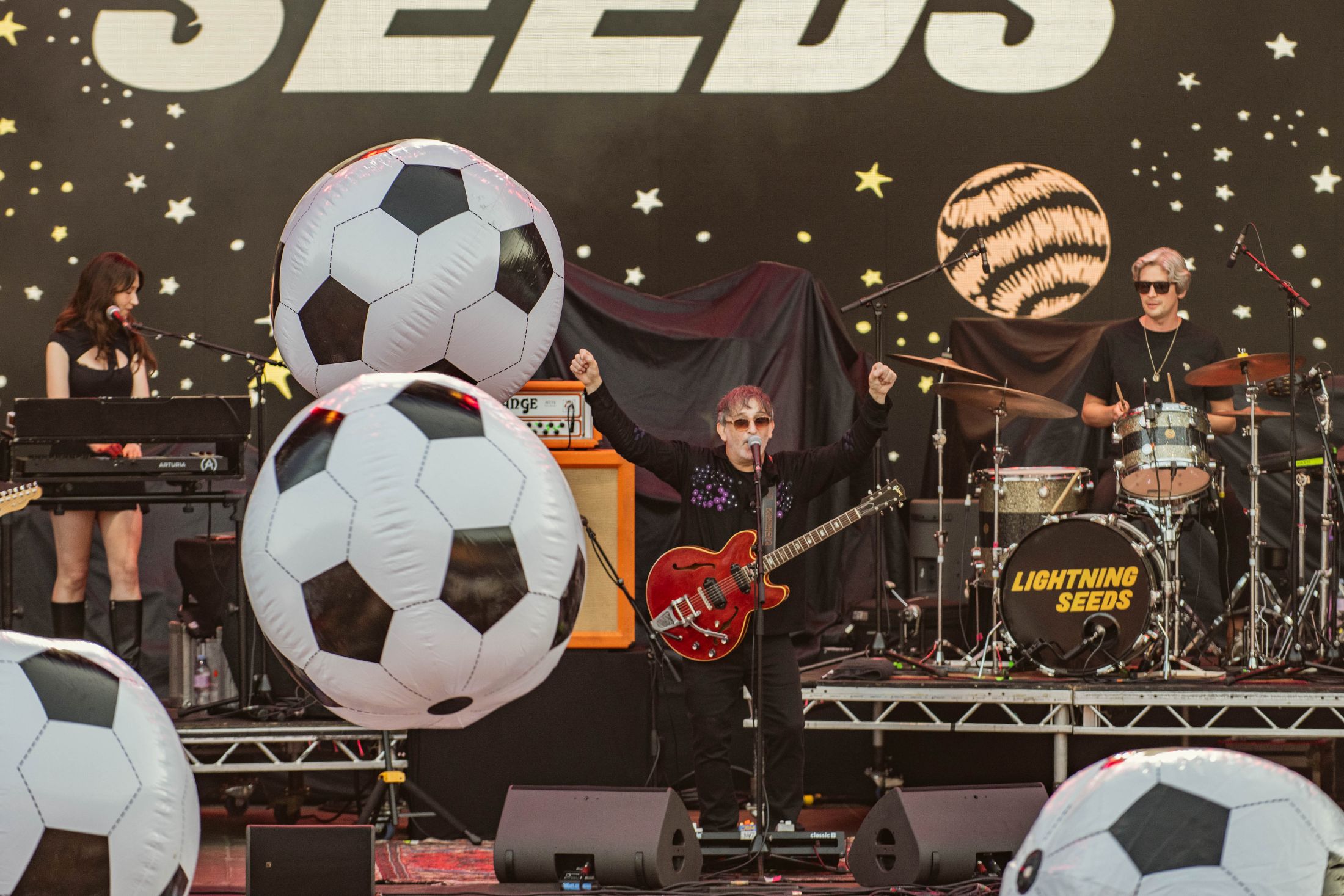 Band performing on stage with large inflatable footballs and starry backdrop