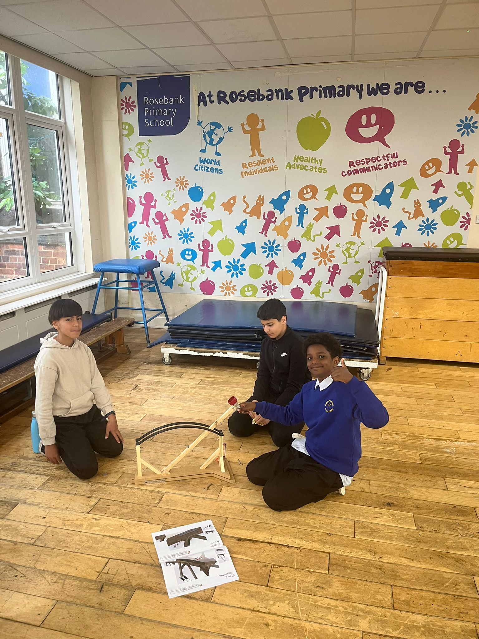 Children assembling a wooden catapult in a school gym