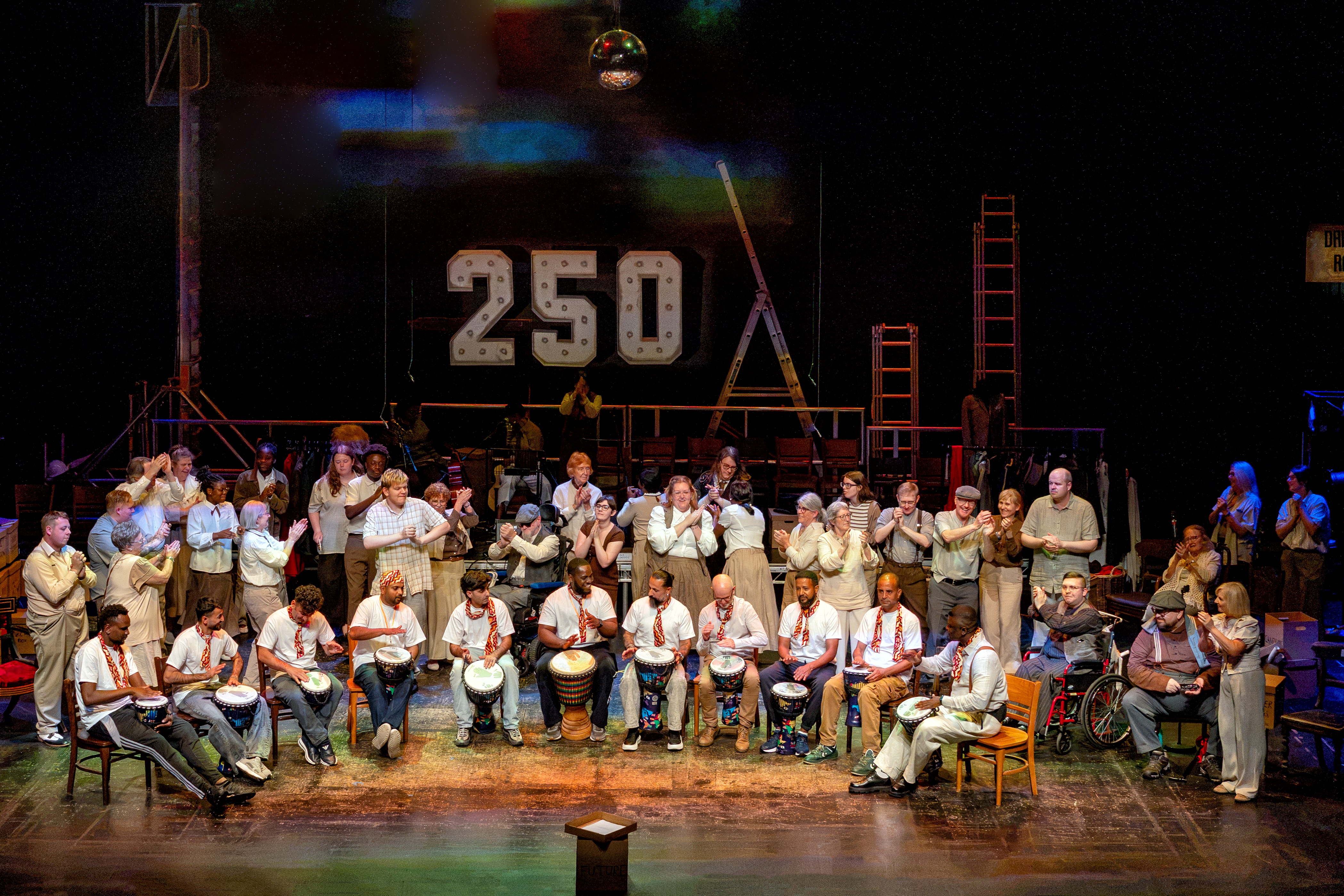 Diverse drumming group performing on stage with large 250 backdrop