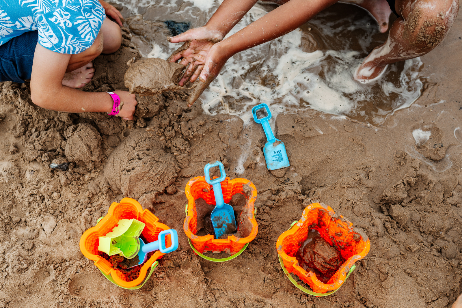 Children playing with sand and colourful buckets on a beach