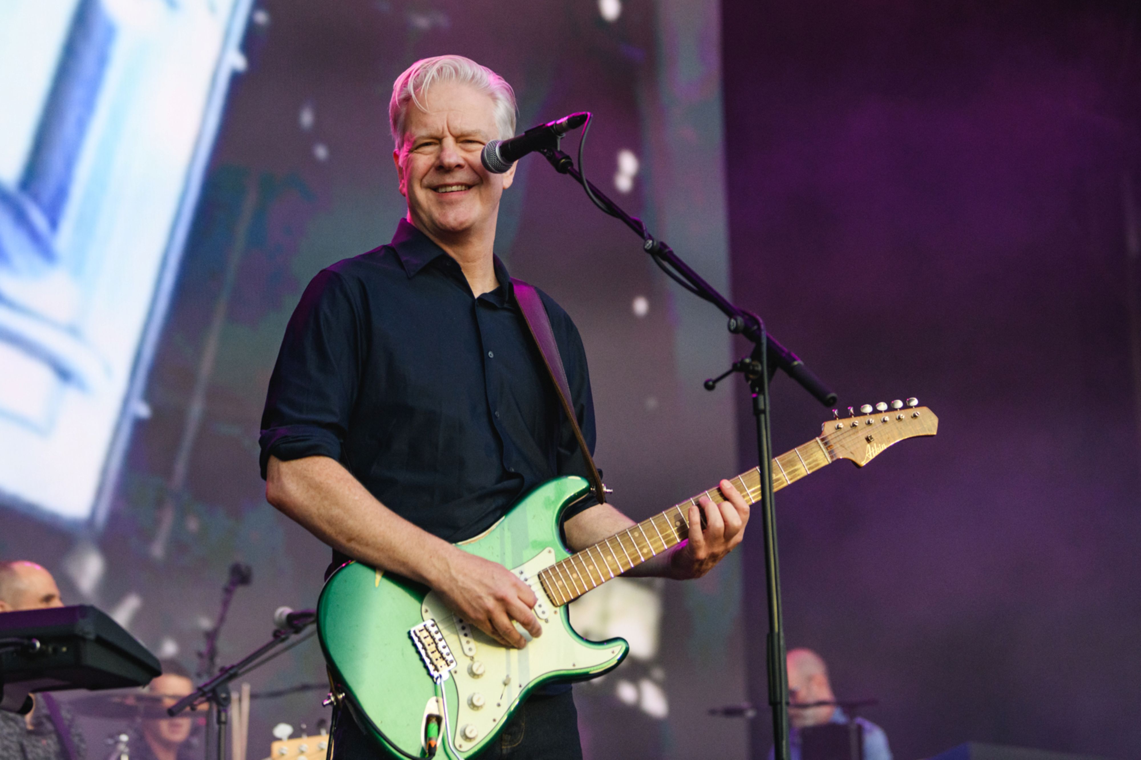 Musician playing green electric guitar on stage with purple lighting