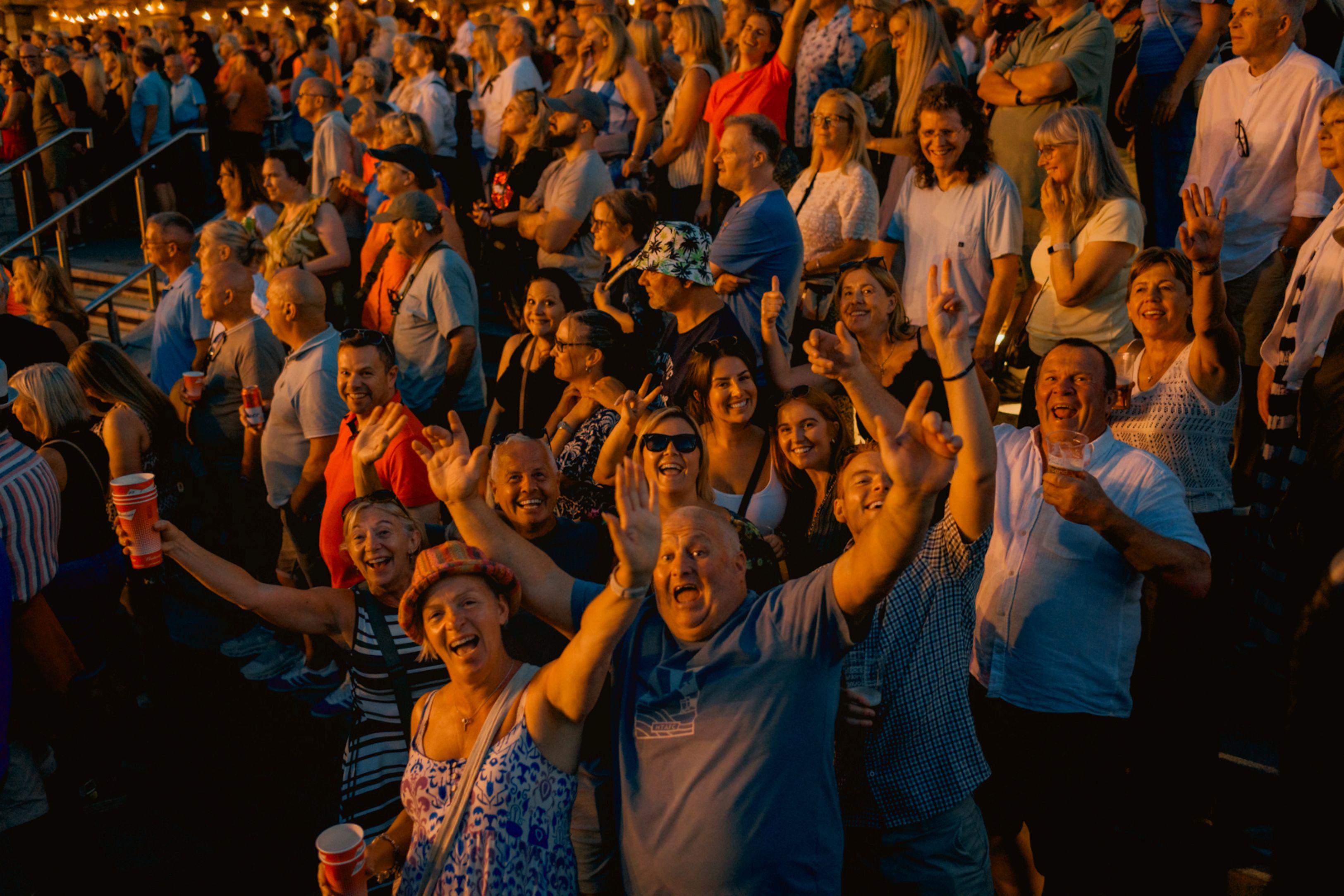 Crowd enjoying an outdoor evening event with festive lighting