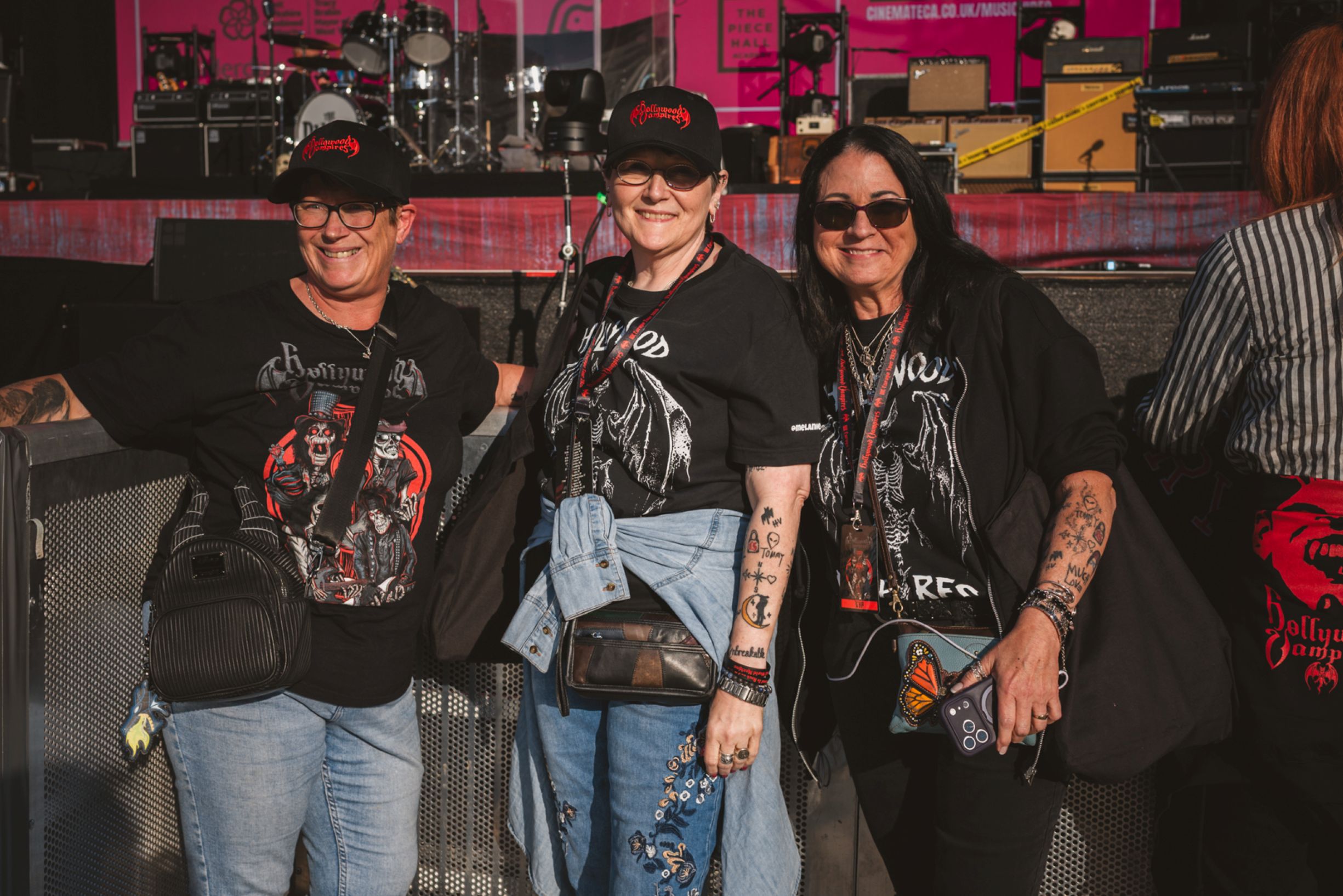 Three women in black t-shirts and hats at an outdoor concert