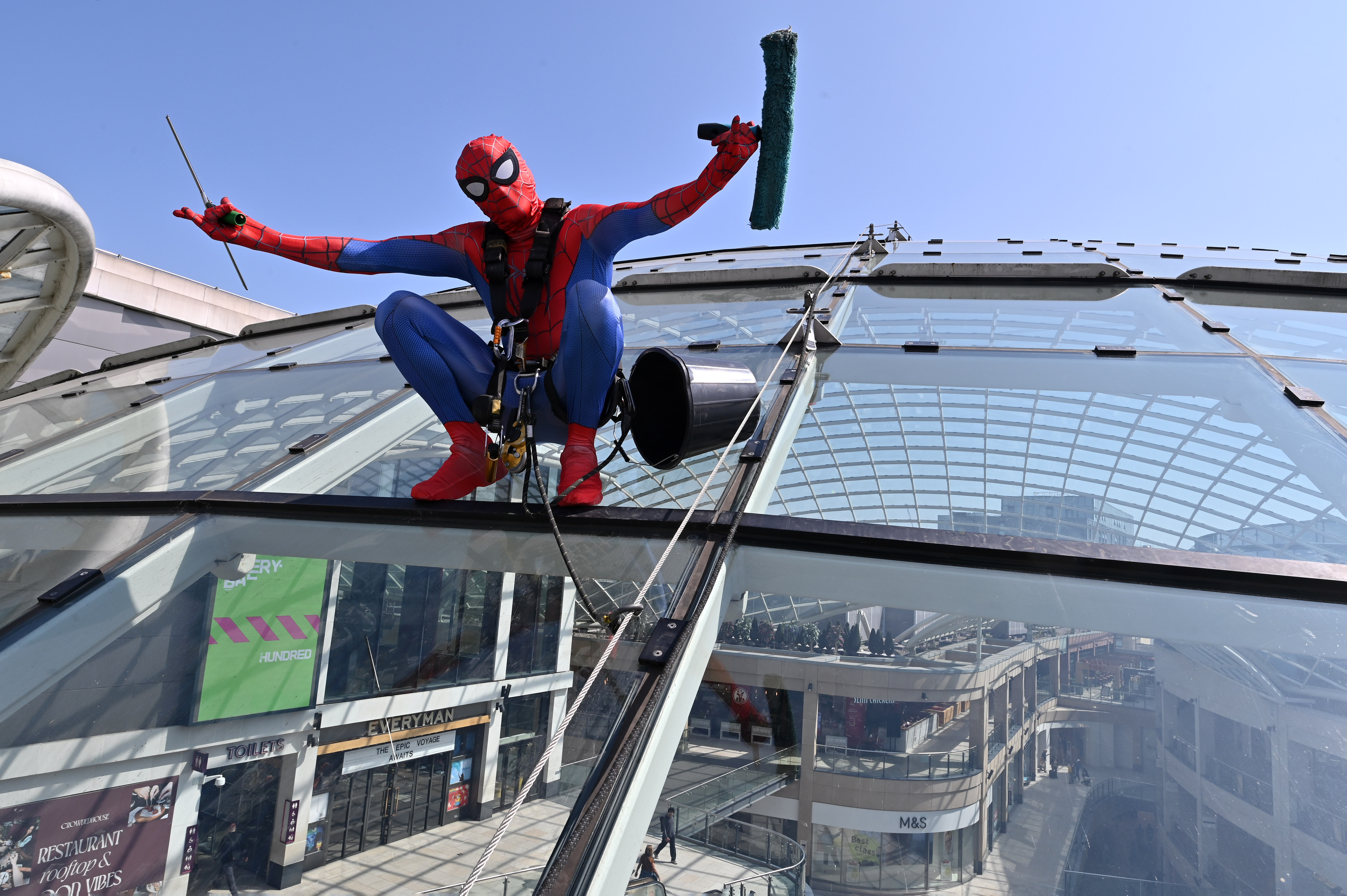Person in superhero costume cleaning glass roof of shopping centre