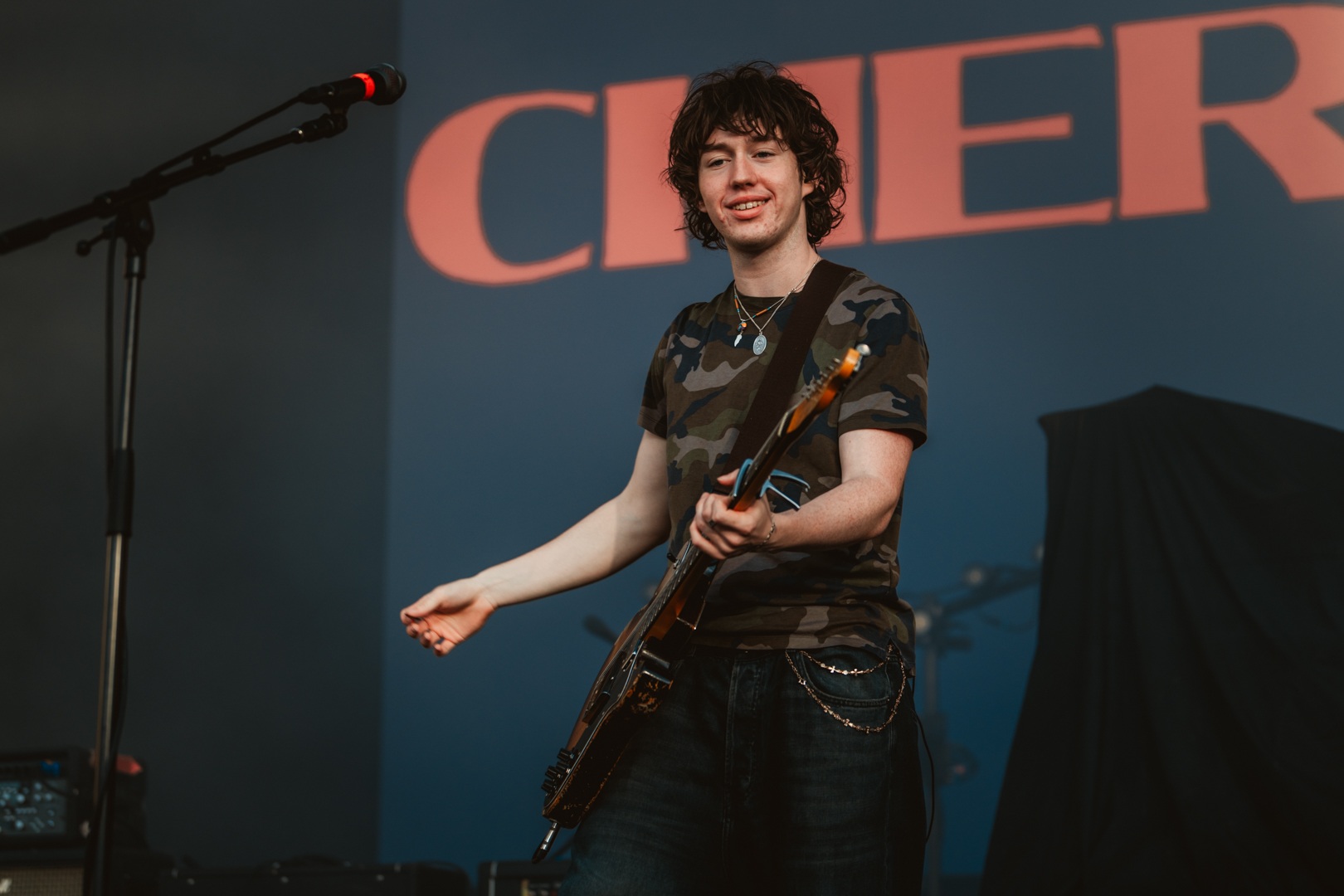 Musician on stage with guitar and microphone, blue backdrop