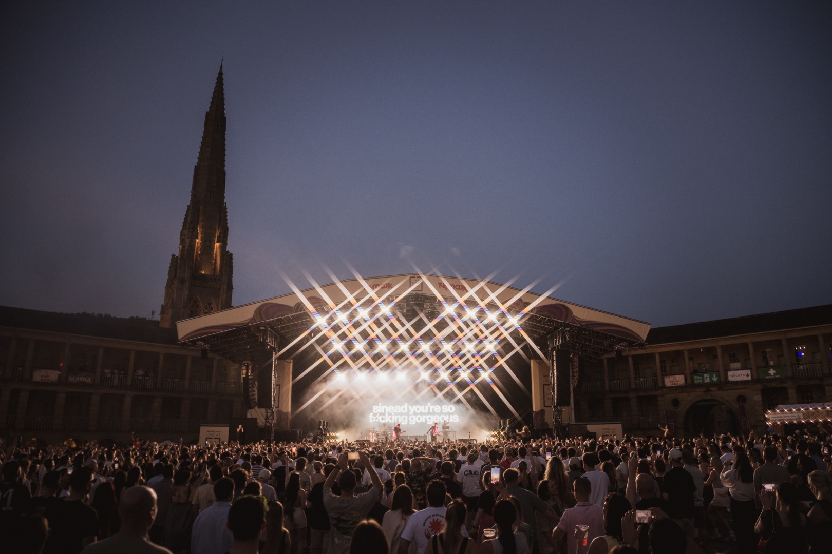 Crowd at outdoor concert with illuminated stage and spire