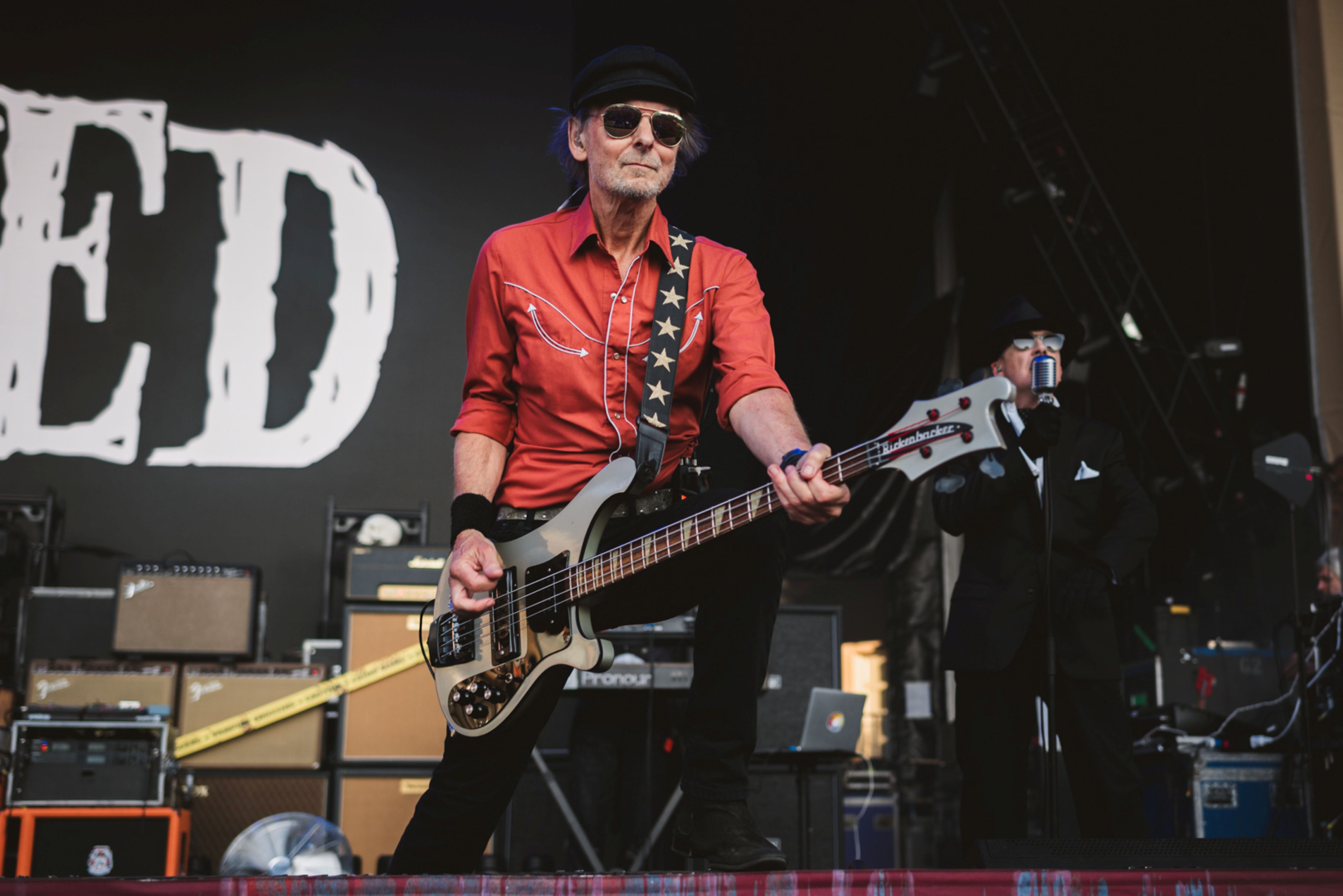 Musician wearing red shirt and hat playing electric bass on stage