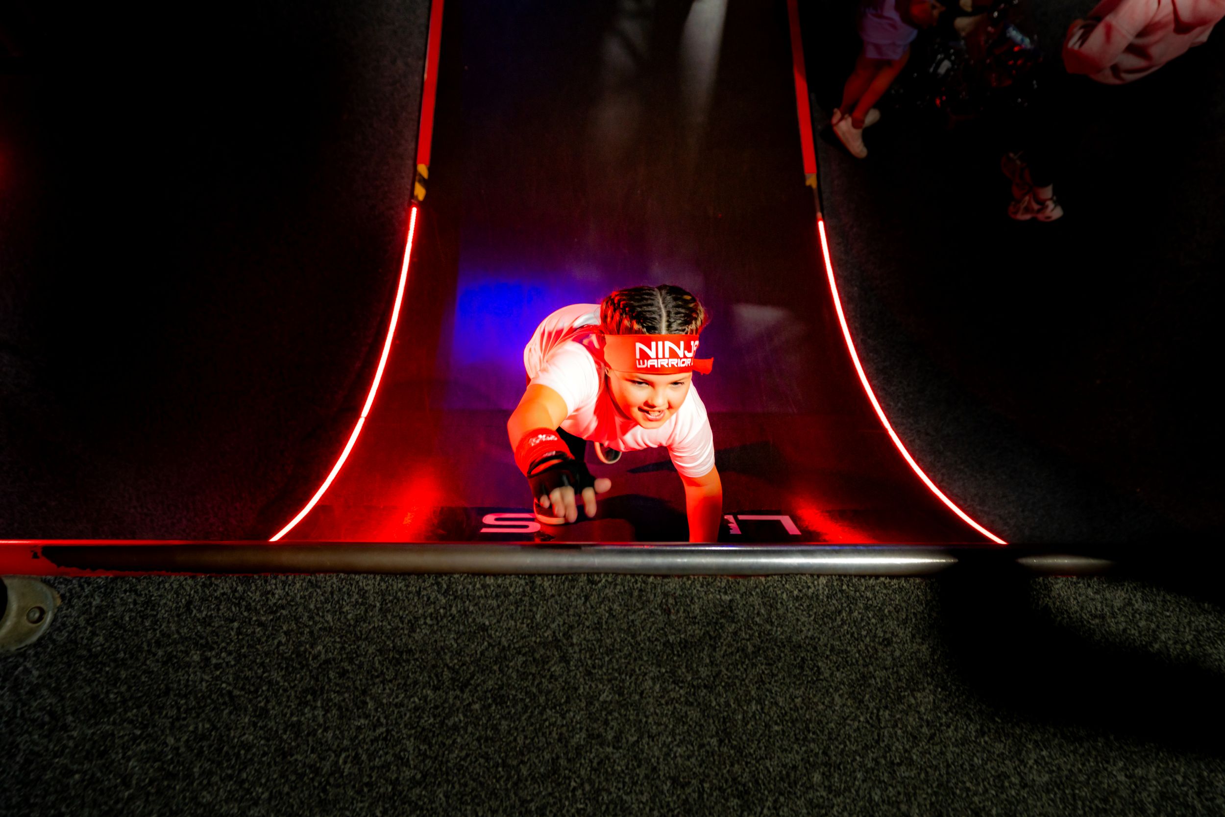 Child climbing a neon-lit obstacle course in an indoor venue