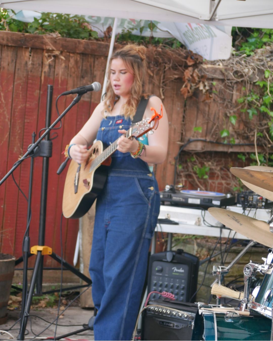 Young woman in denim overalls playing guitar on outdoor stage