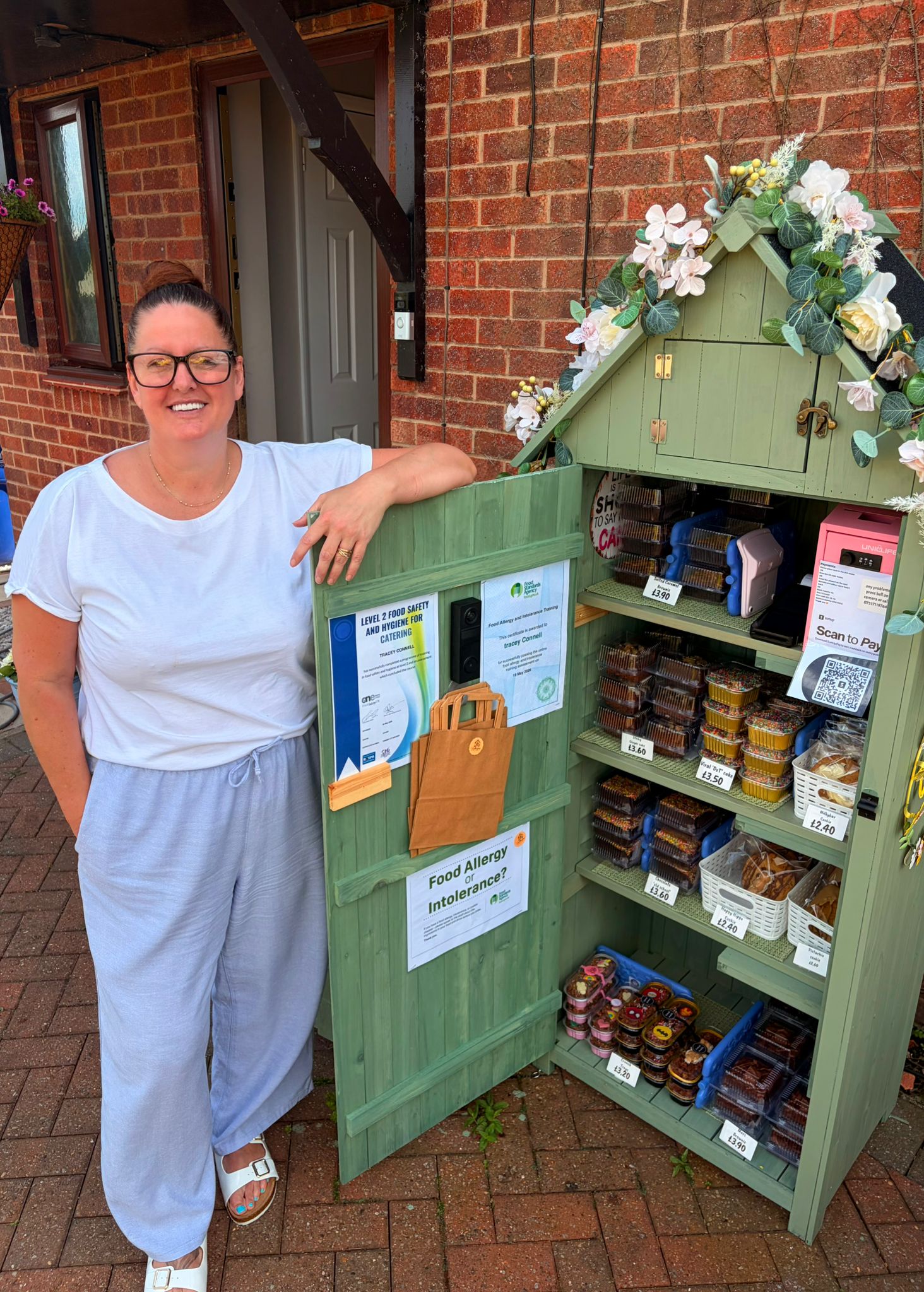 Woman standing beside a green outdoor pantry filled with food items