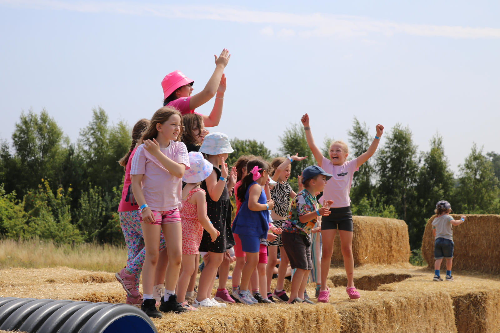 Children playing and cheering on hay bales in a sunny field