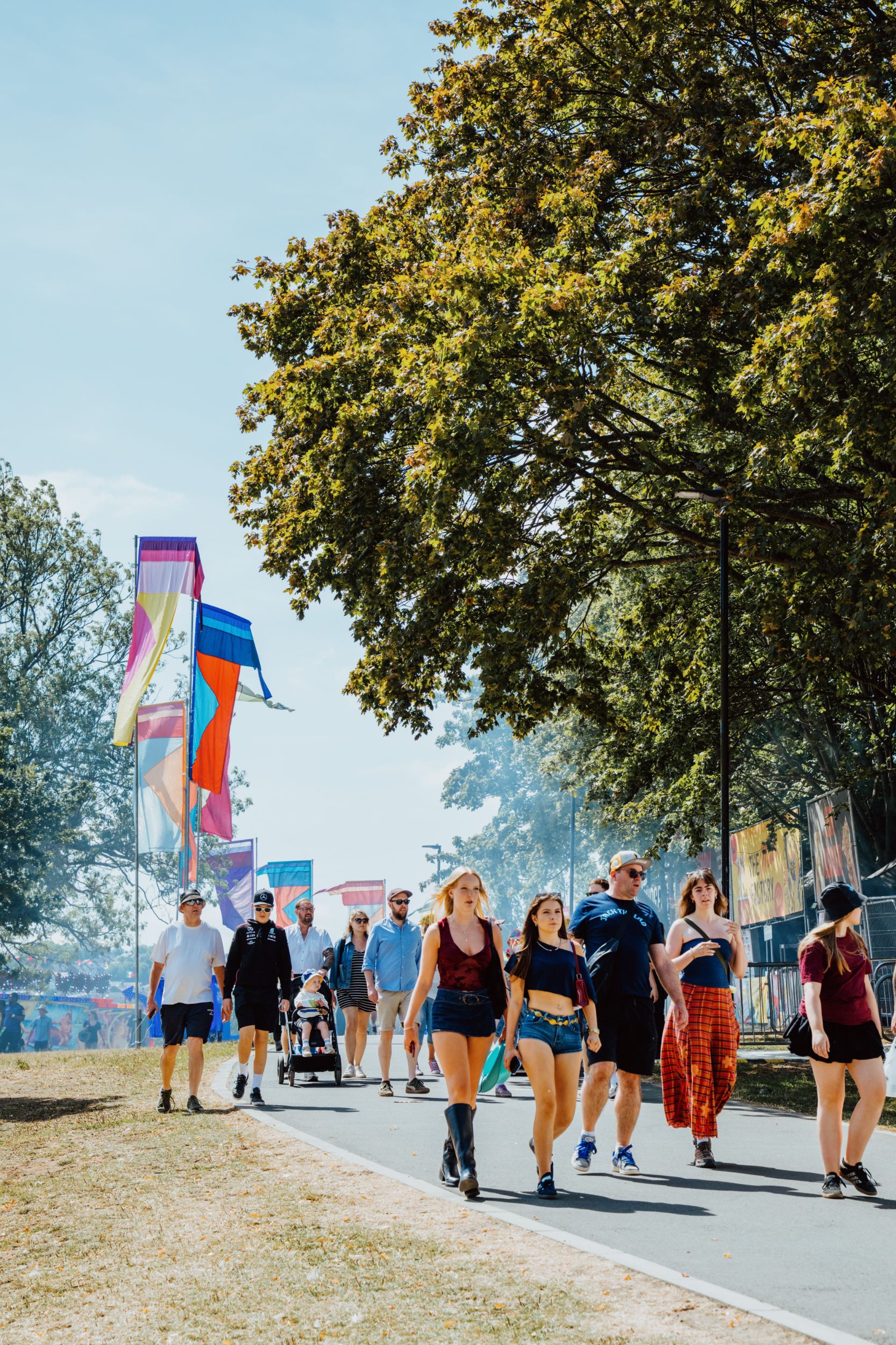 People strolling along a tree-lined path with colourful flags