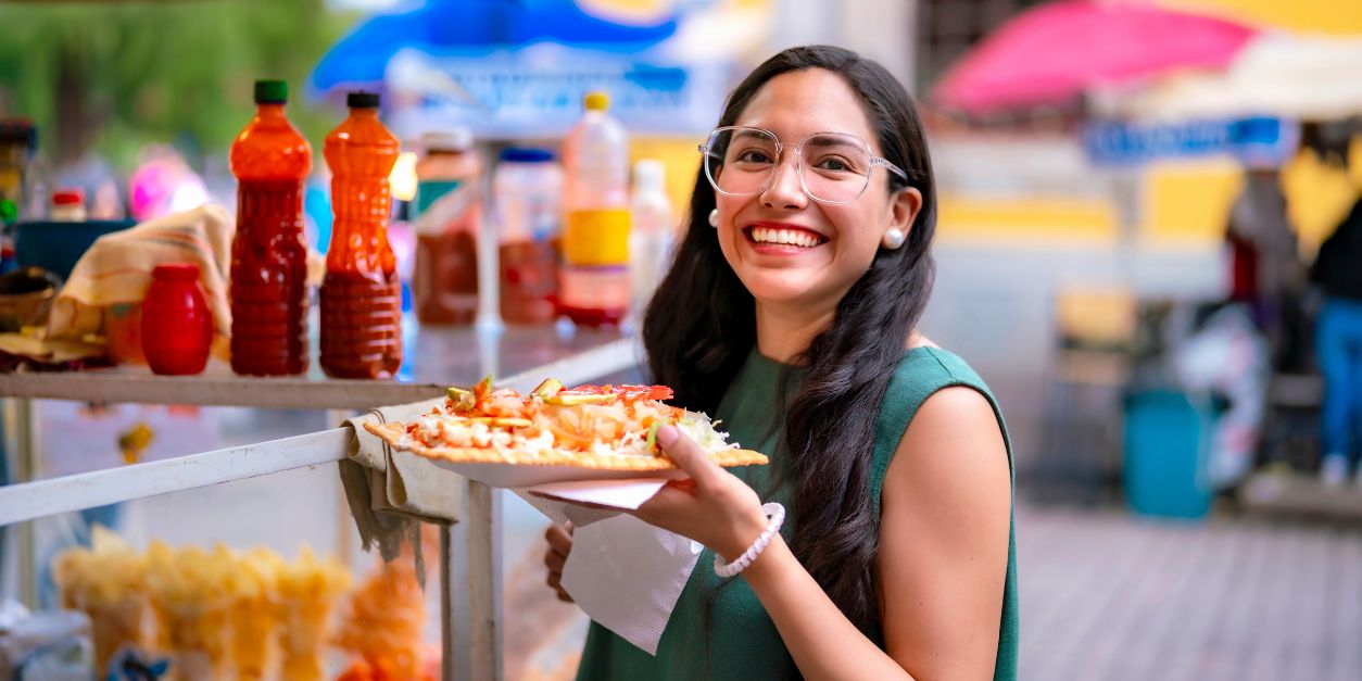 Smiling woman holding a plate of street food at an outdoor market