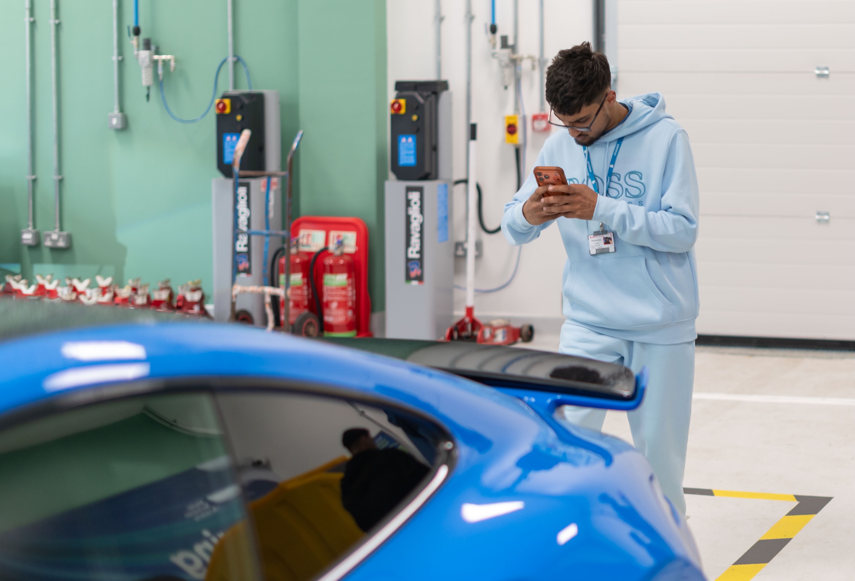 Young man in light blue tracksuit checking phone by blue sports car