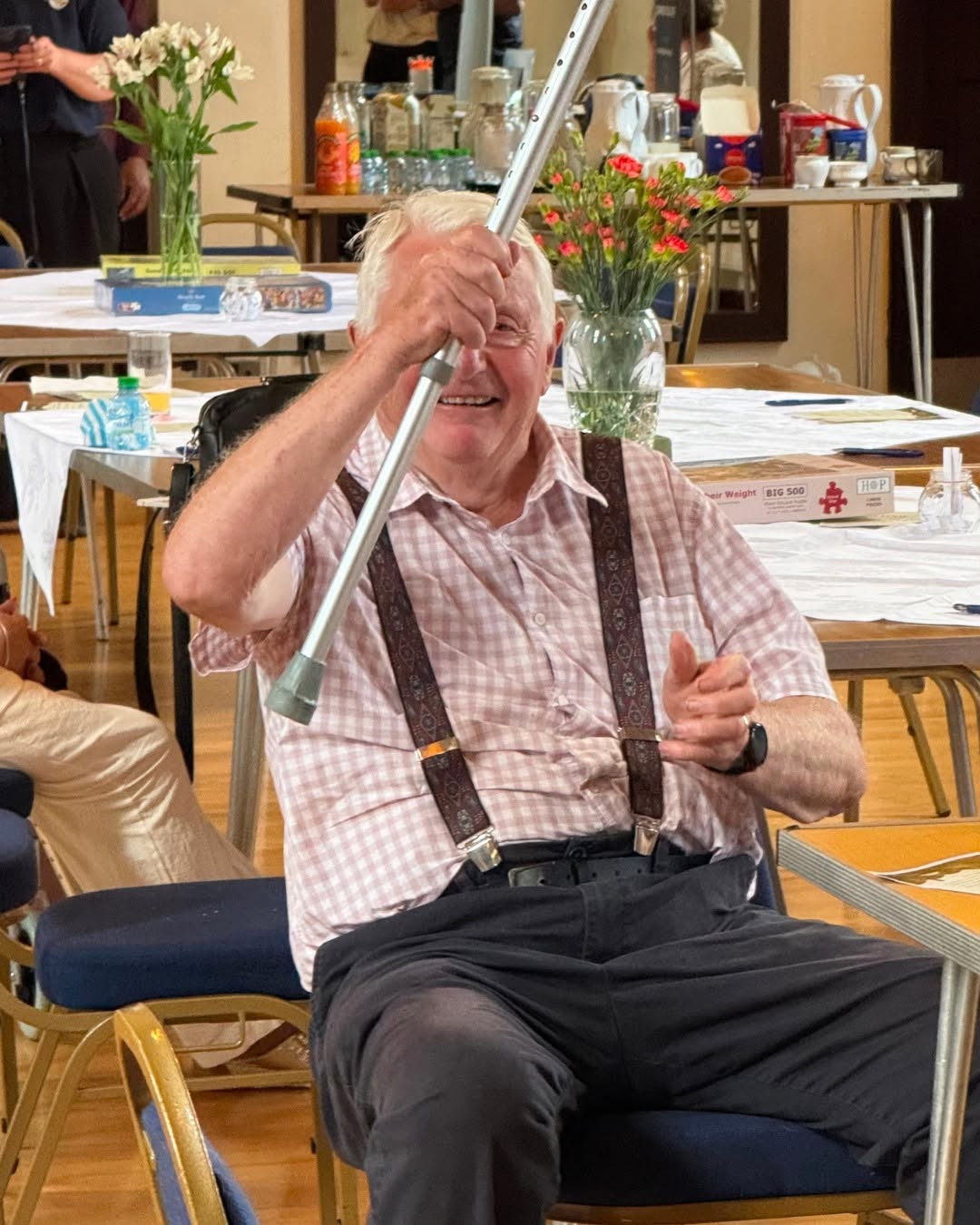 Elderly man smiling and holding a walking stick indoors