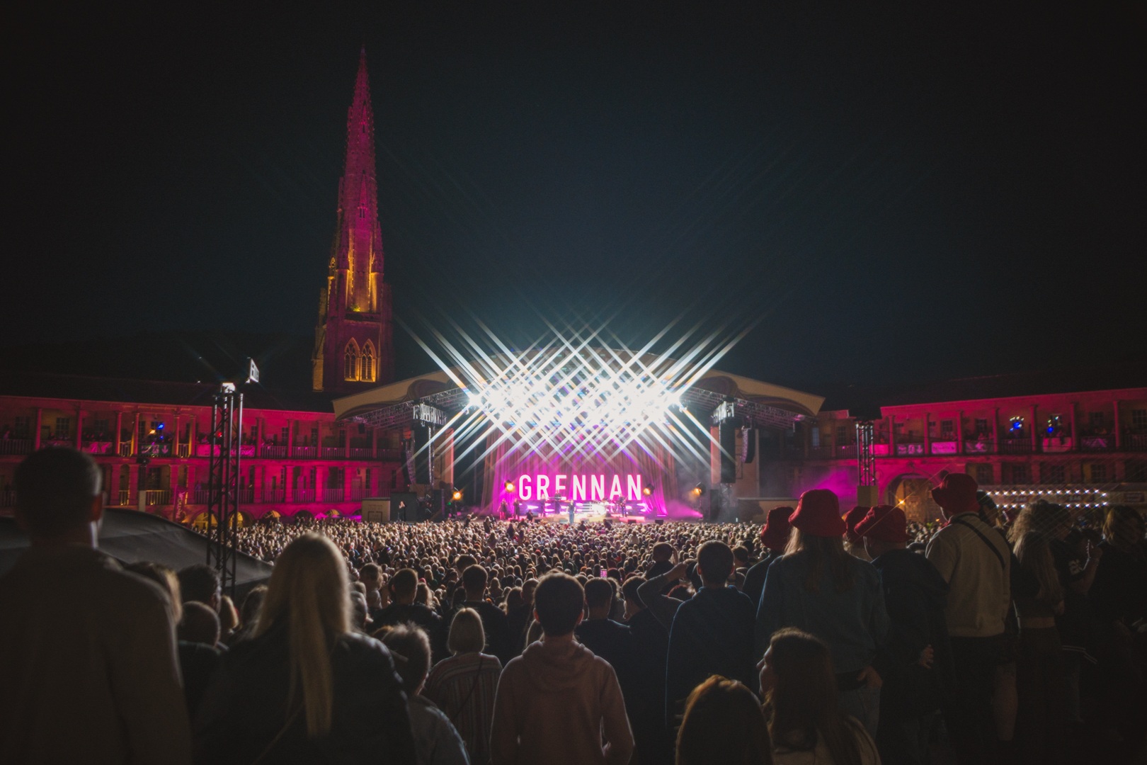 Crowd at outdoor night concert with illuminated stage and church spire