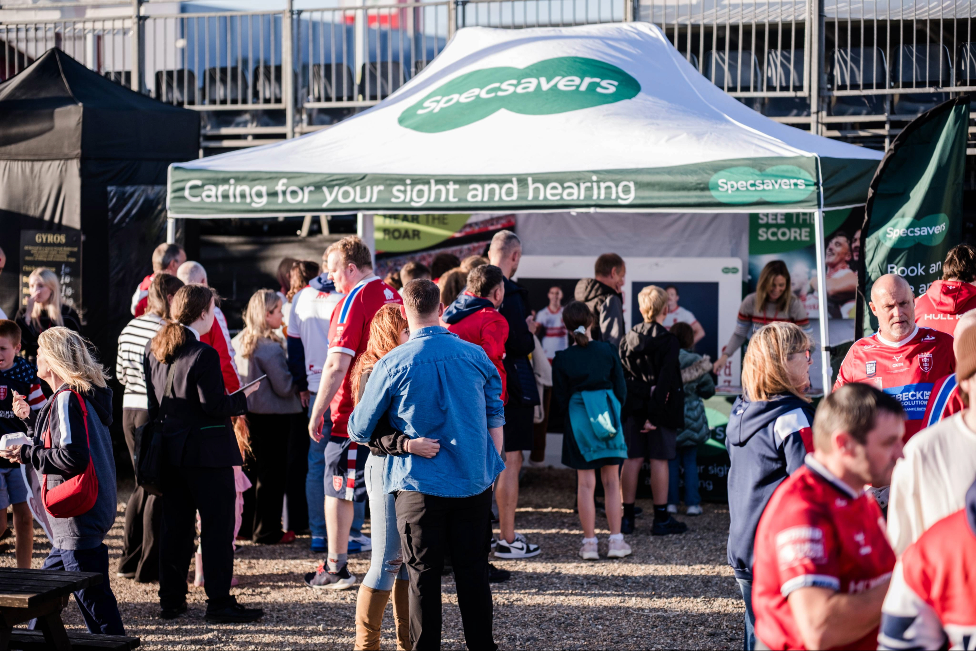 Crowd at an outdoor event by a white Specsavers tent