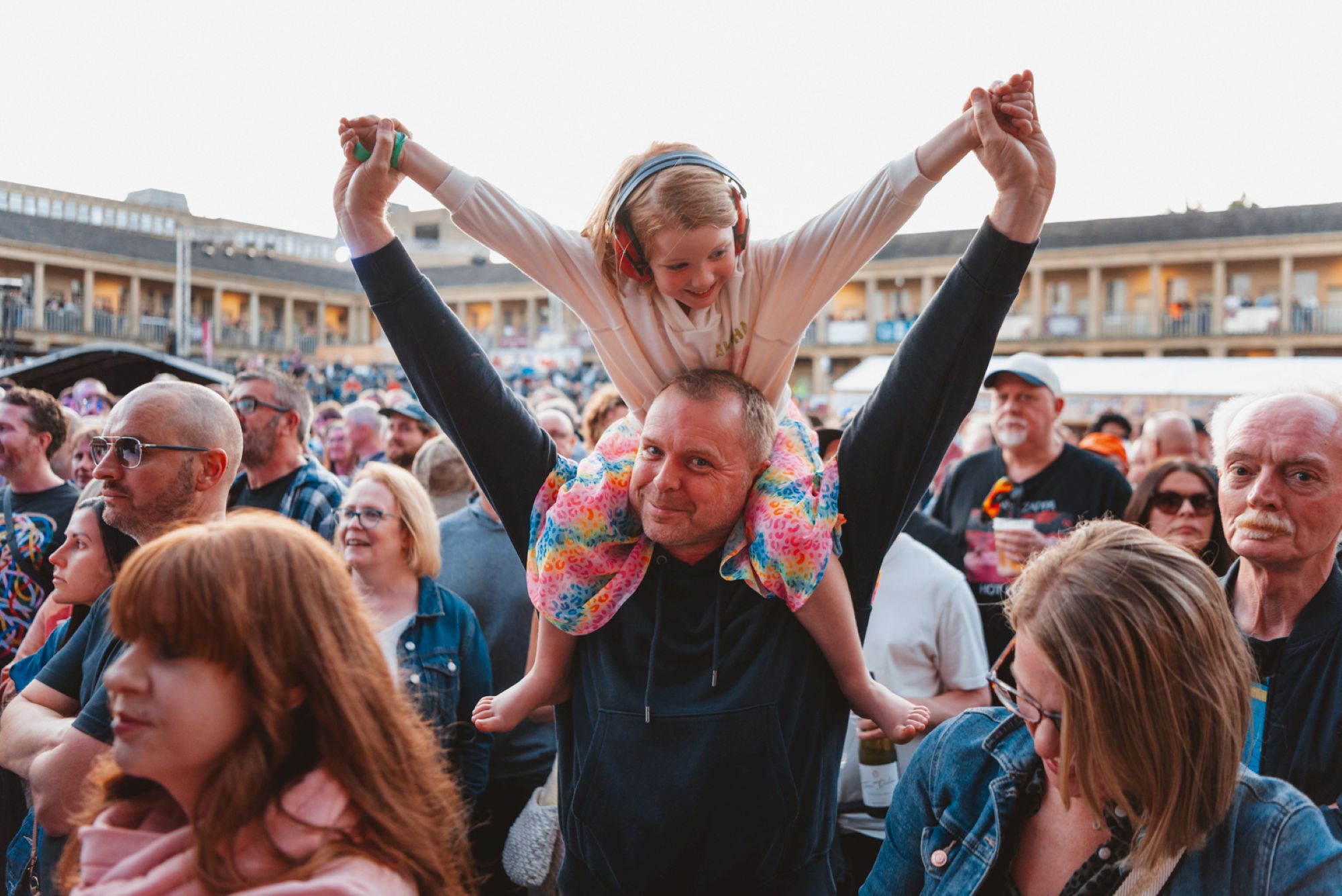 Smiling man with child on shoulders at lively outdoor festival