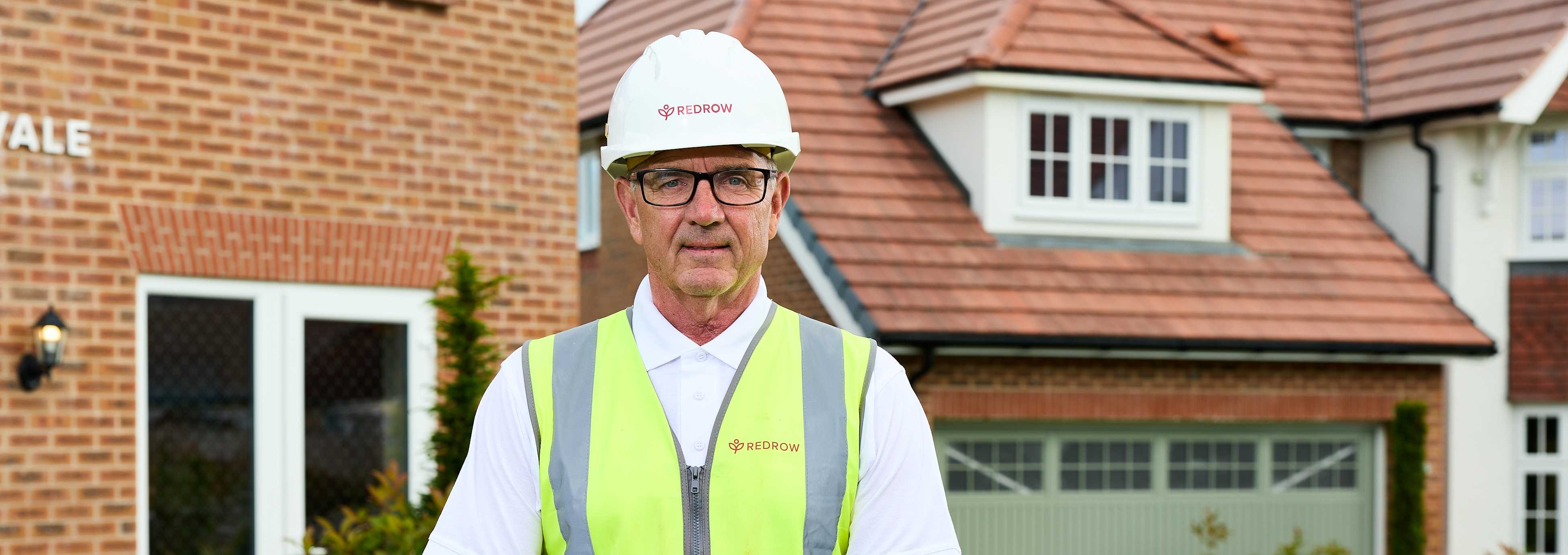 Builder in high-vis vest and hard hat in front of new house